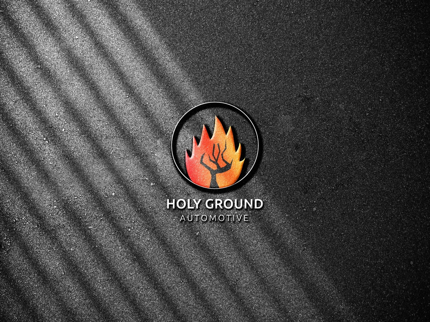 A black circular emblem with a stylized tree inside flames, placed on a dark textured background with diagonal light reflections. Below, the text reads "HOLY GROUND AUTOMOTIVE."