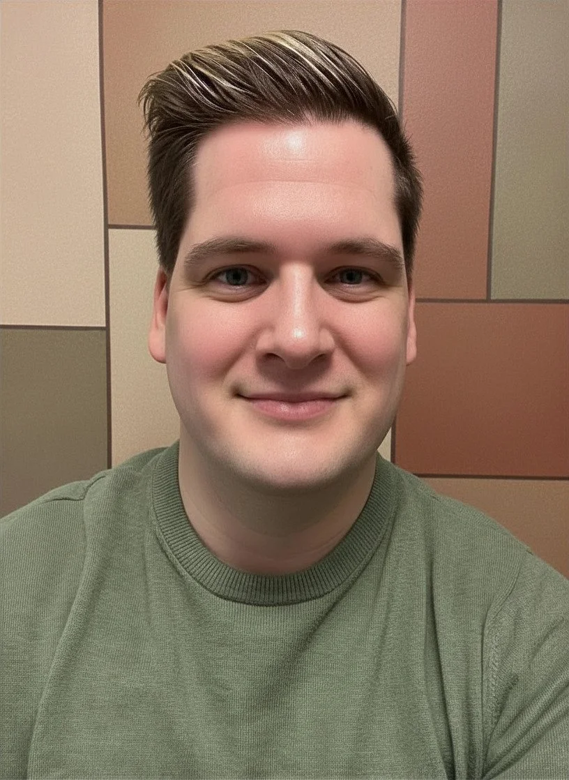 A young man with short, neatly combed brown hair, smiling, wearing a green crewneck sweatshirt, in front of a colorful tiled wall.