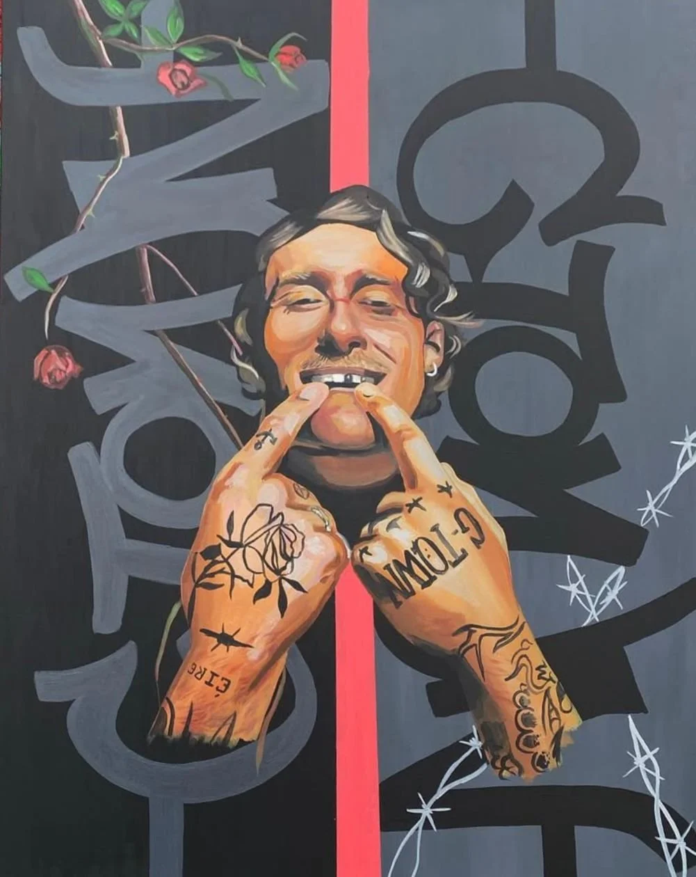 A painting of a smiling man with tattoos on his hands and fingers, holding his fingers to his mouth and making a gesture. The background features graffiti-style art and floral elements.
