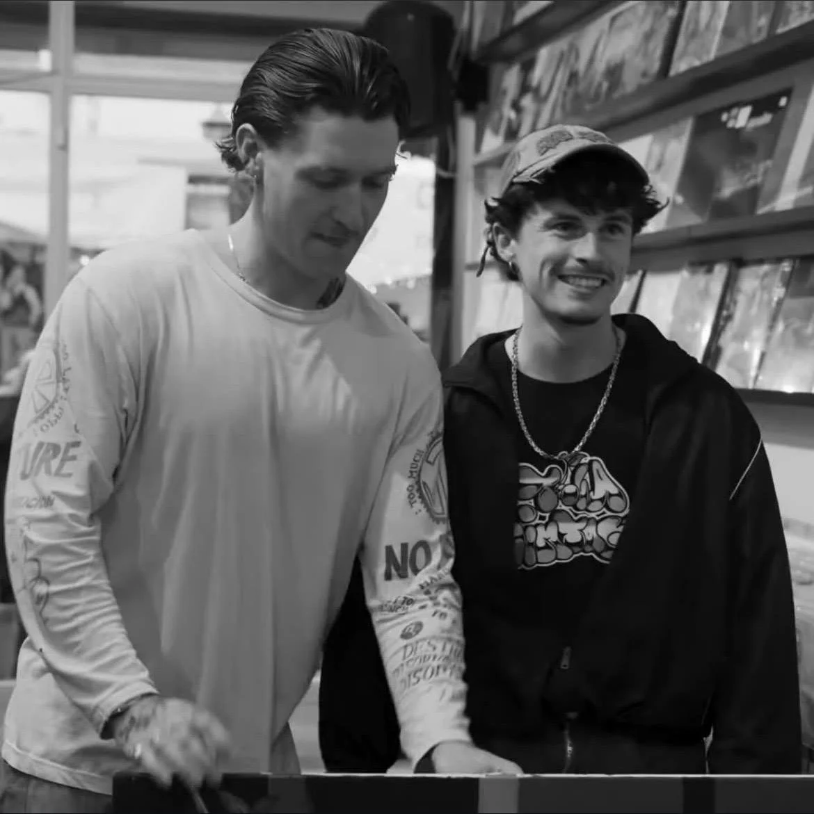 Two young men smiling and looking at something on a table in a record store.