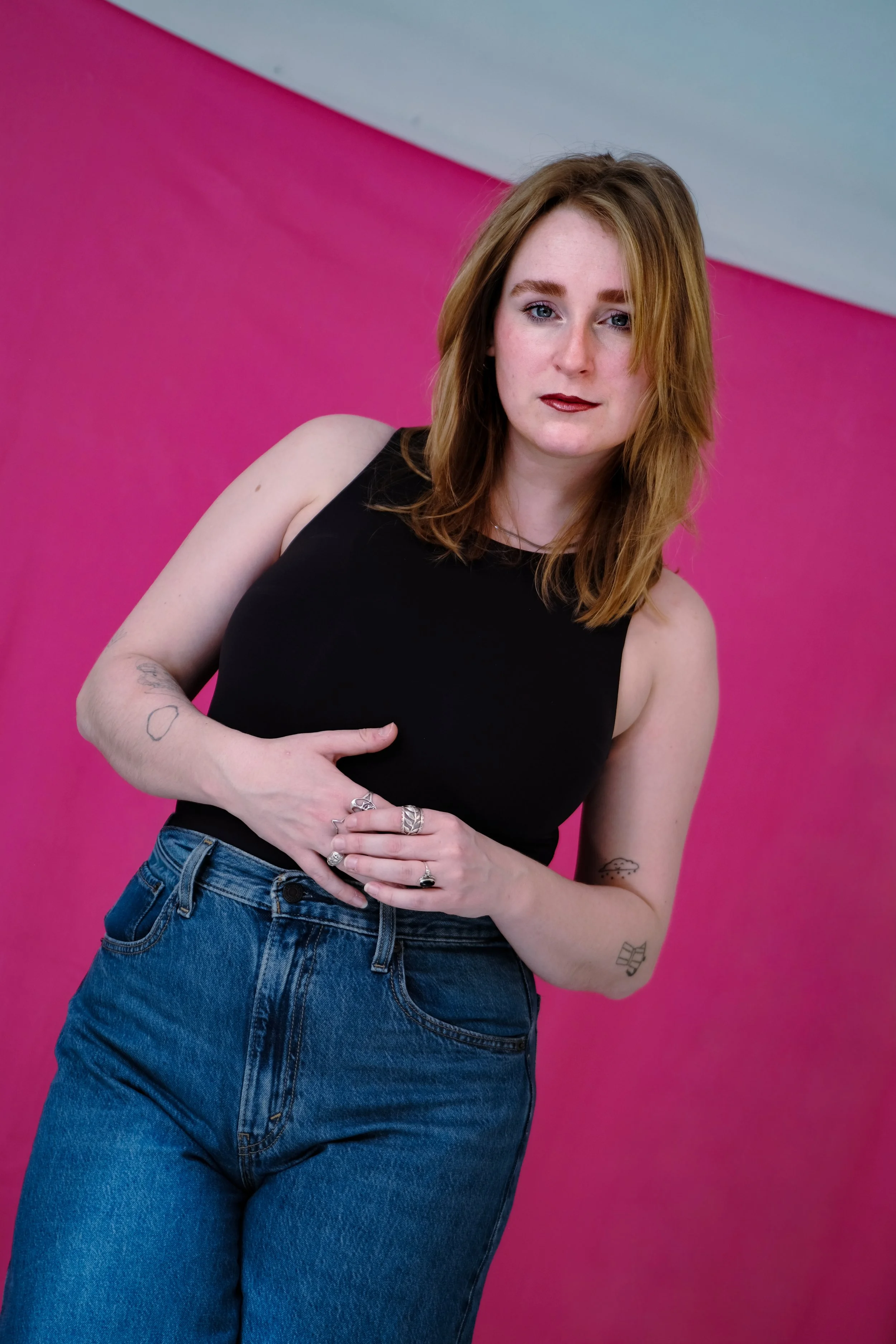 Marie Gedicke: rote Haare, schwarzes Top und blauen Jeans vor pinker Wand.