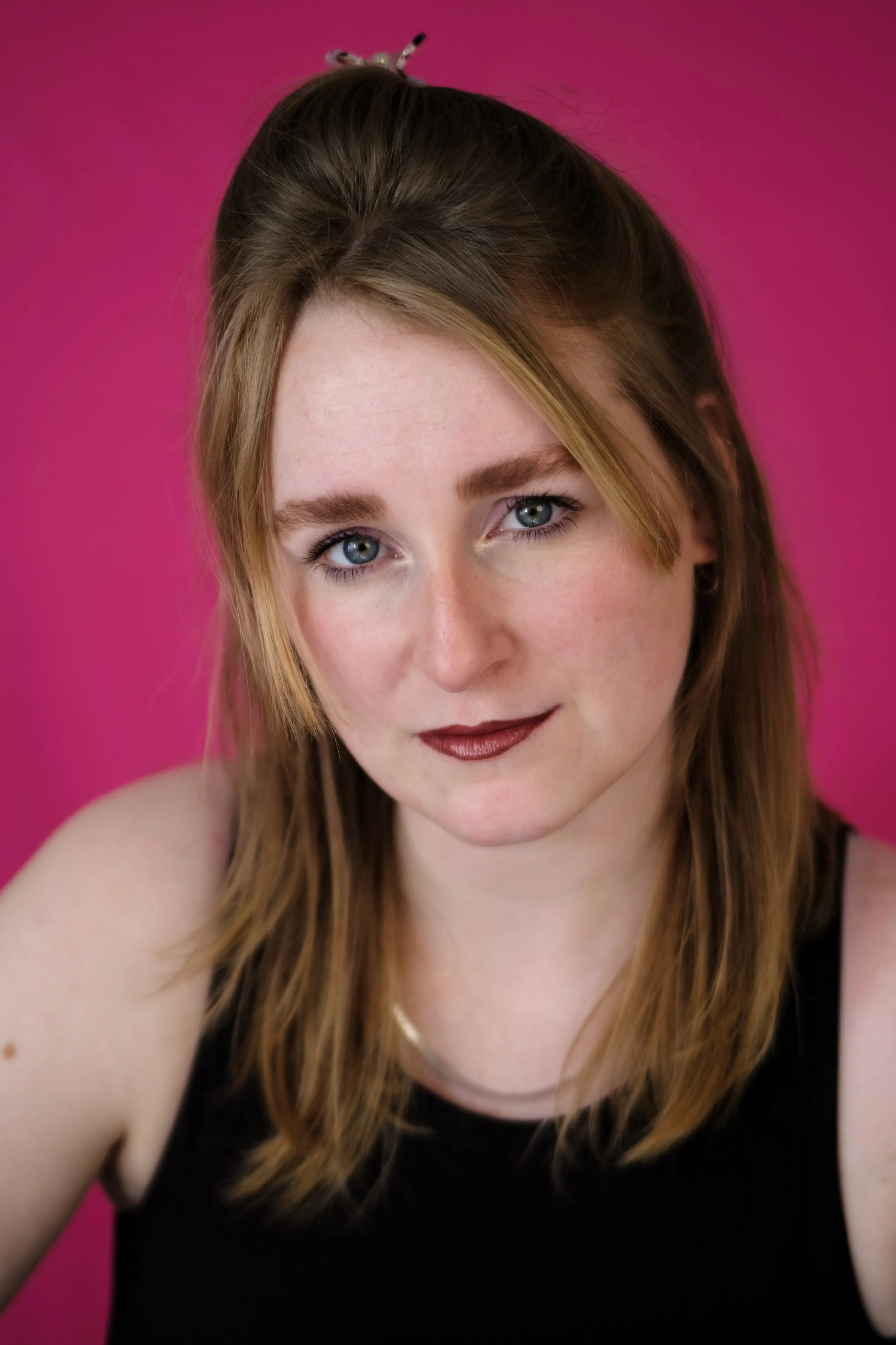 Porträt Marie Gedicke vor pinkem Hintergrund, mit braunen Haaren und dunklen Lippenstift.
