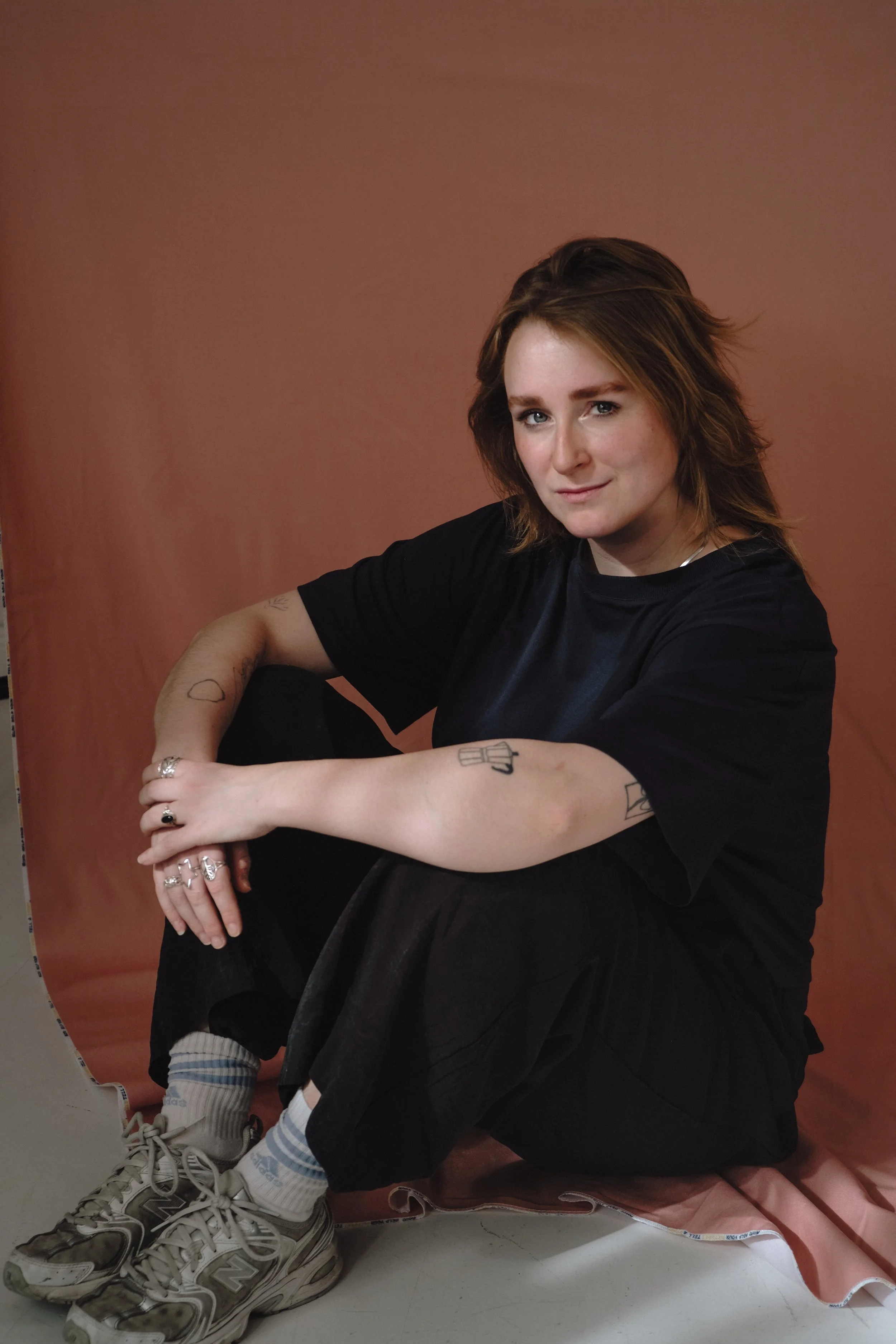 Marie Gedicke, sitzend, trägt schwarze Kleidung vor einem braunen Hintergrund.
