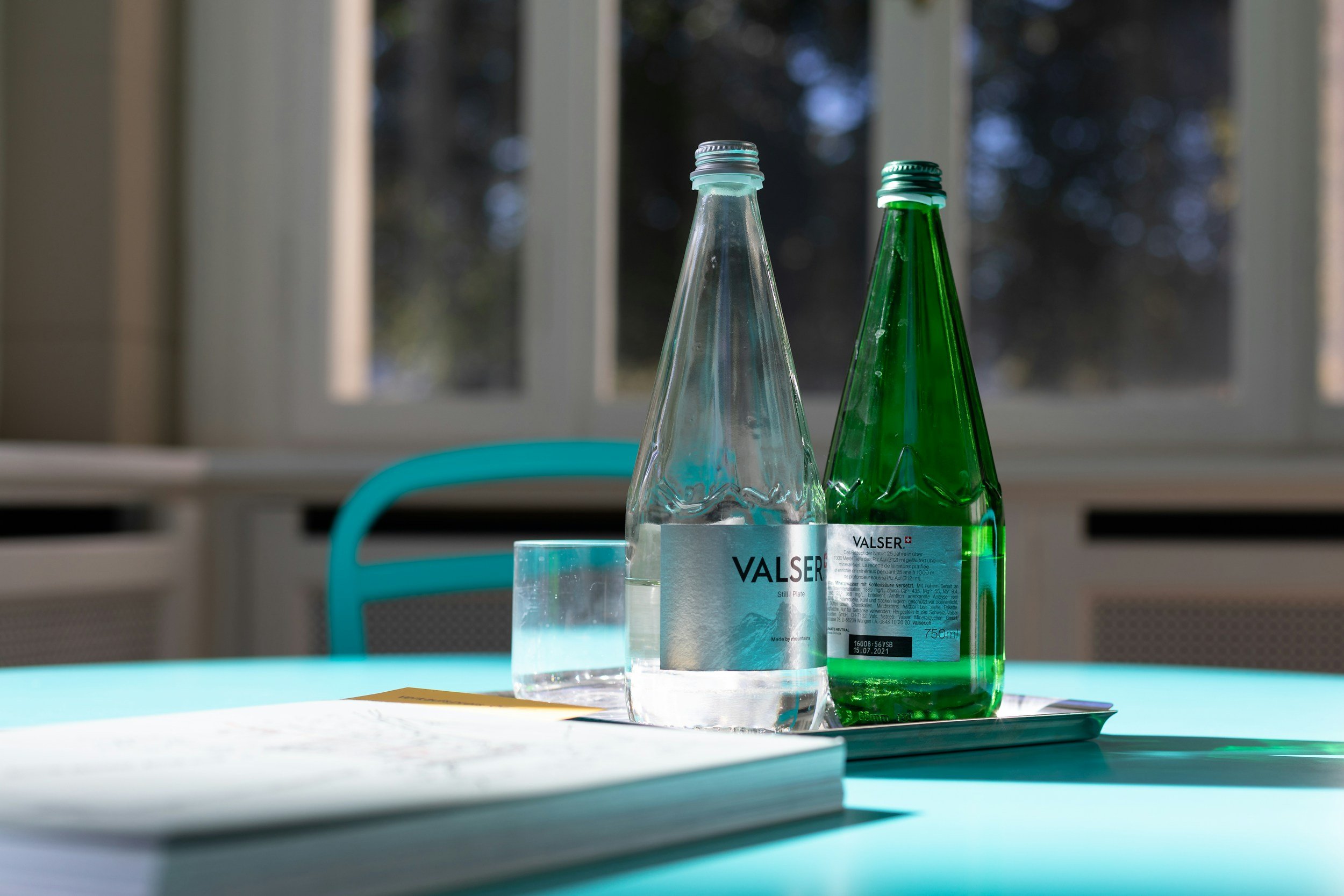 Zwei Glasflaschen, eine leere und eine gefüllte, auf einem Tablett neben einem Glas Wasser und einem Buch.