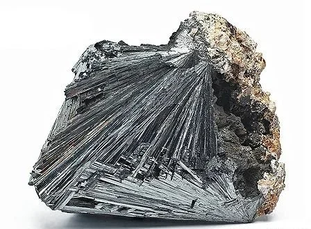 Ein metallischer Kristall mit spitzen, welligen Strukturen, teilweise mit einer grauen, groben Mineralhülle