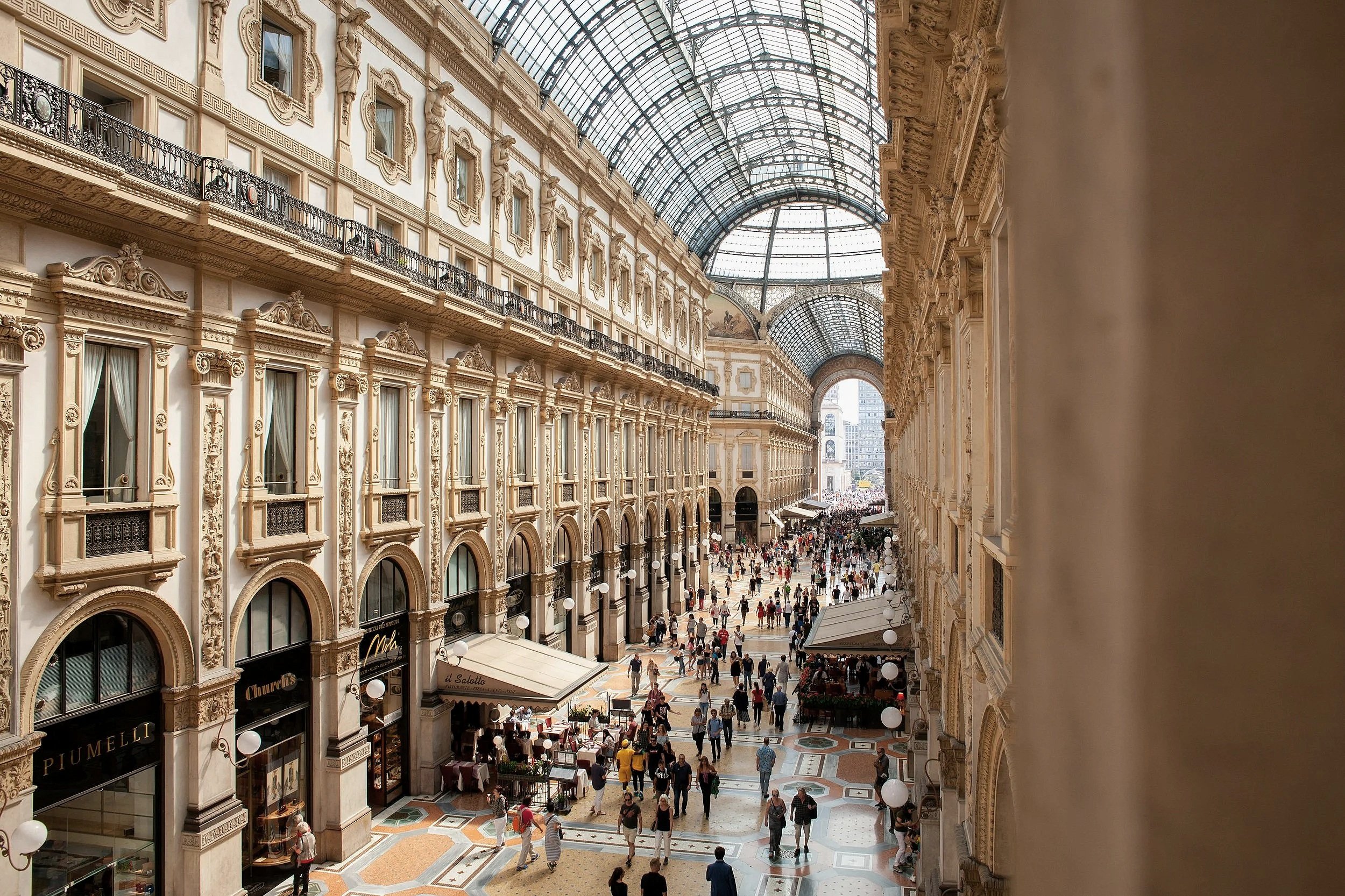 Galleria Vittorio Emanuele II in Milan, Italy, with ornate architecture, a glass roof, and shoppers walking below