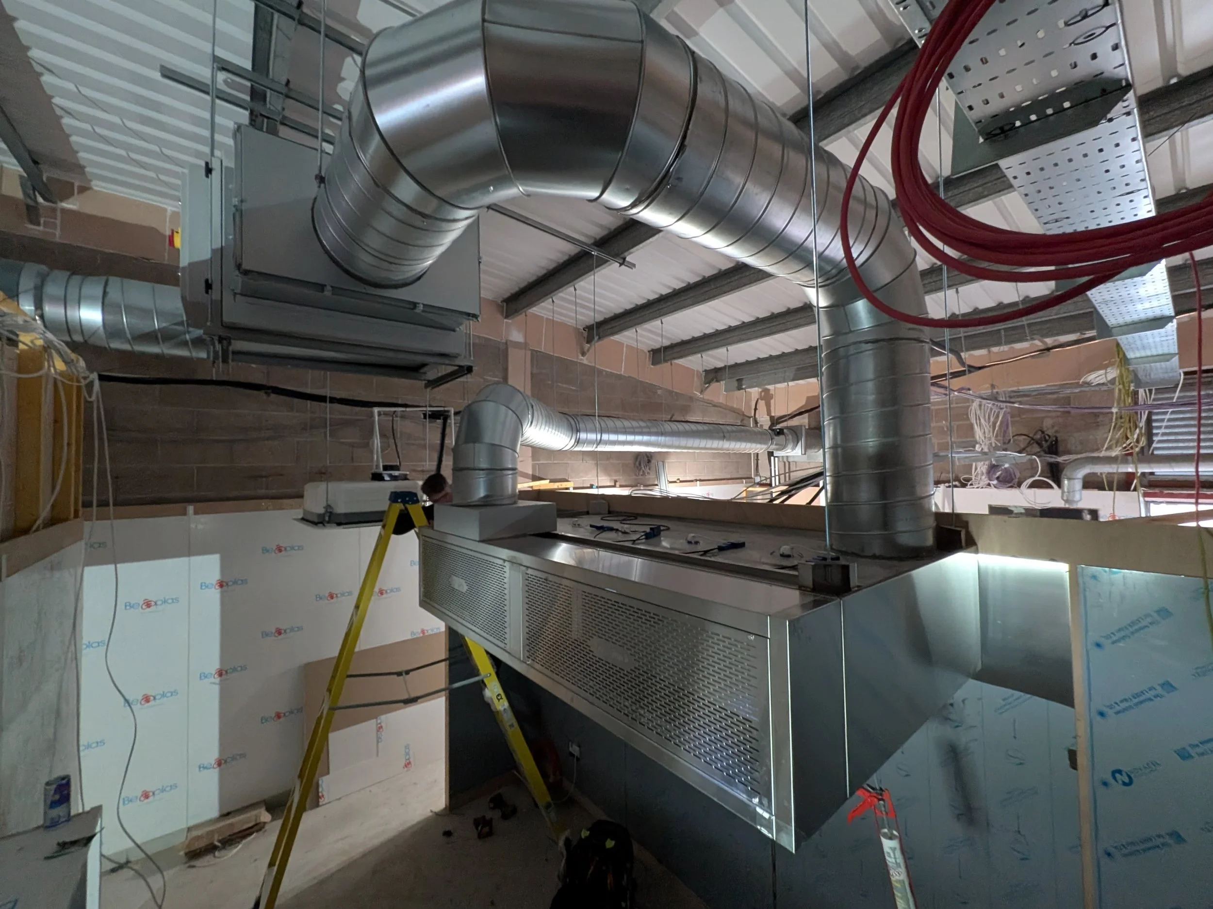 View of an industrial HVAC system installation with large metal ducts, ventilation units, and electrical wiring in a building under construction.