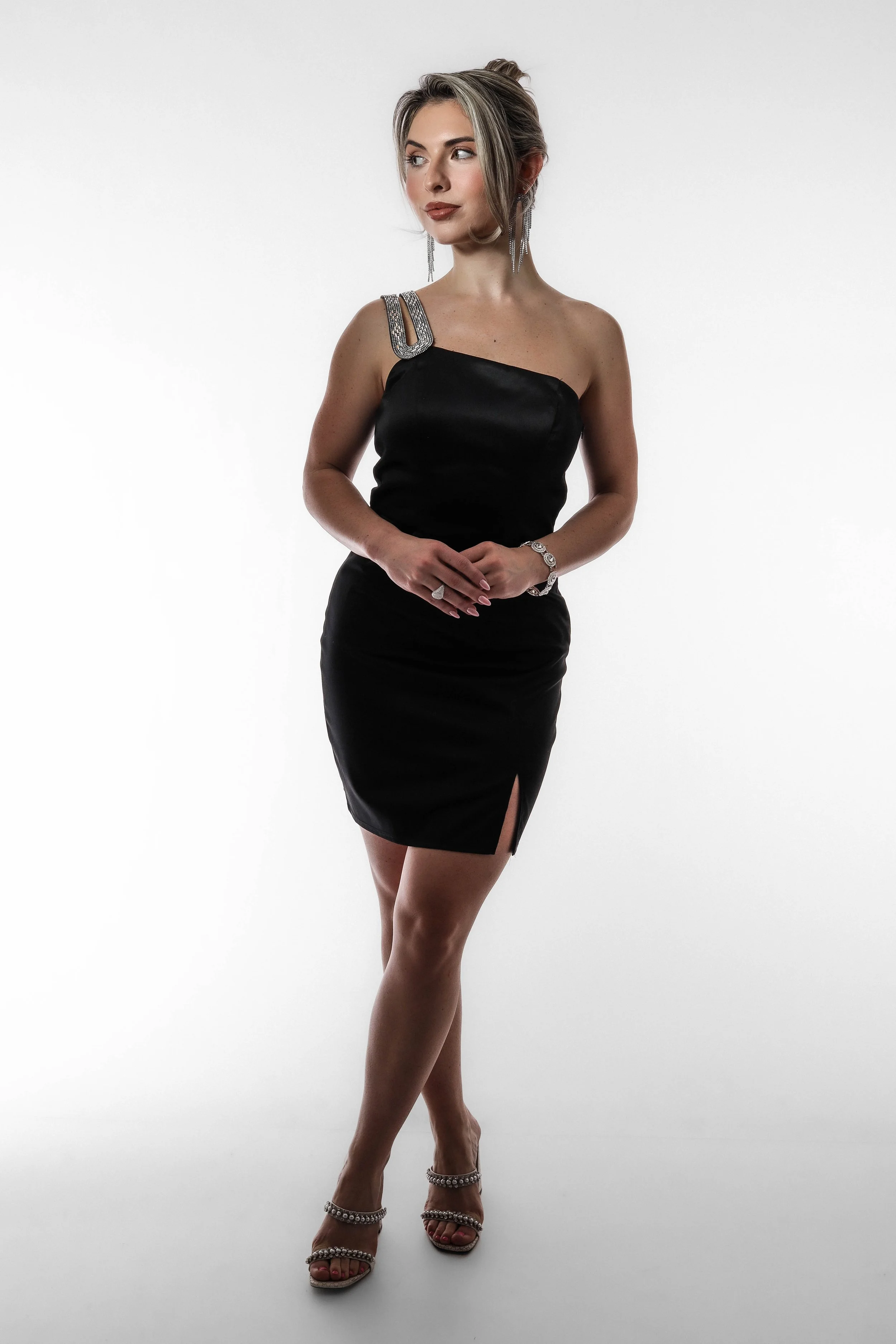 Young woman in black dress with silver jewelry, posing against a white background.