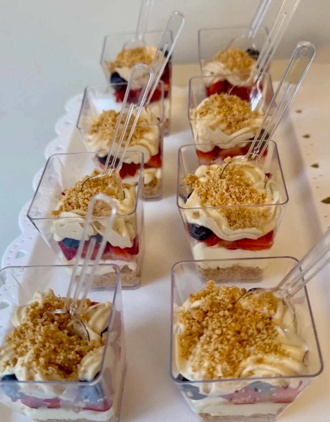 Dessert cups filled with layered strawberries, blueberries, whipped cream, and crumbled topping, arranged in a rectangular container.