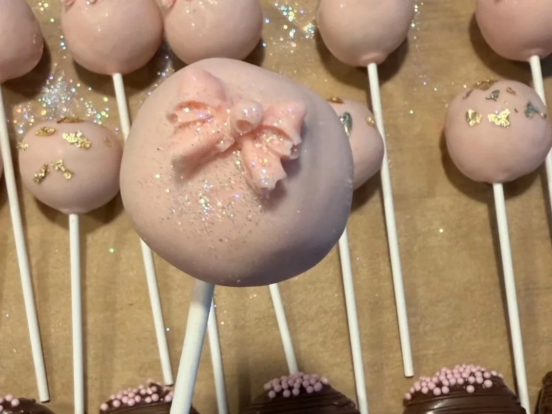Pink cake pops decorated with gold leaf and glitter, arranged on sticks, with a large pink cake pop in the center.