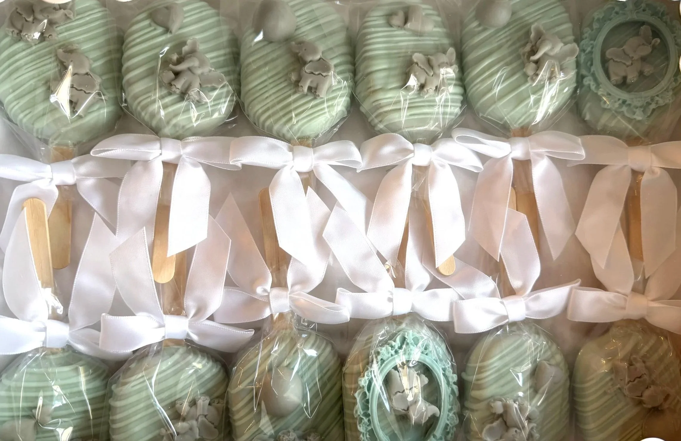 Green and white striped cake pops decorated with teddy bear toppers, wrapped in clear plastic with white ribbons.