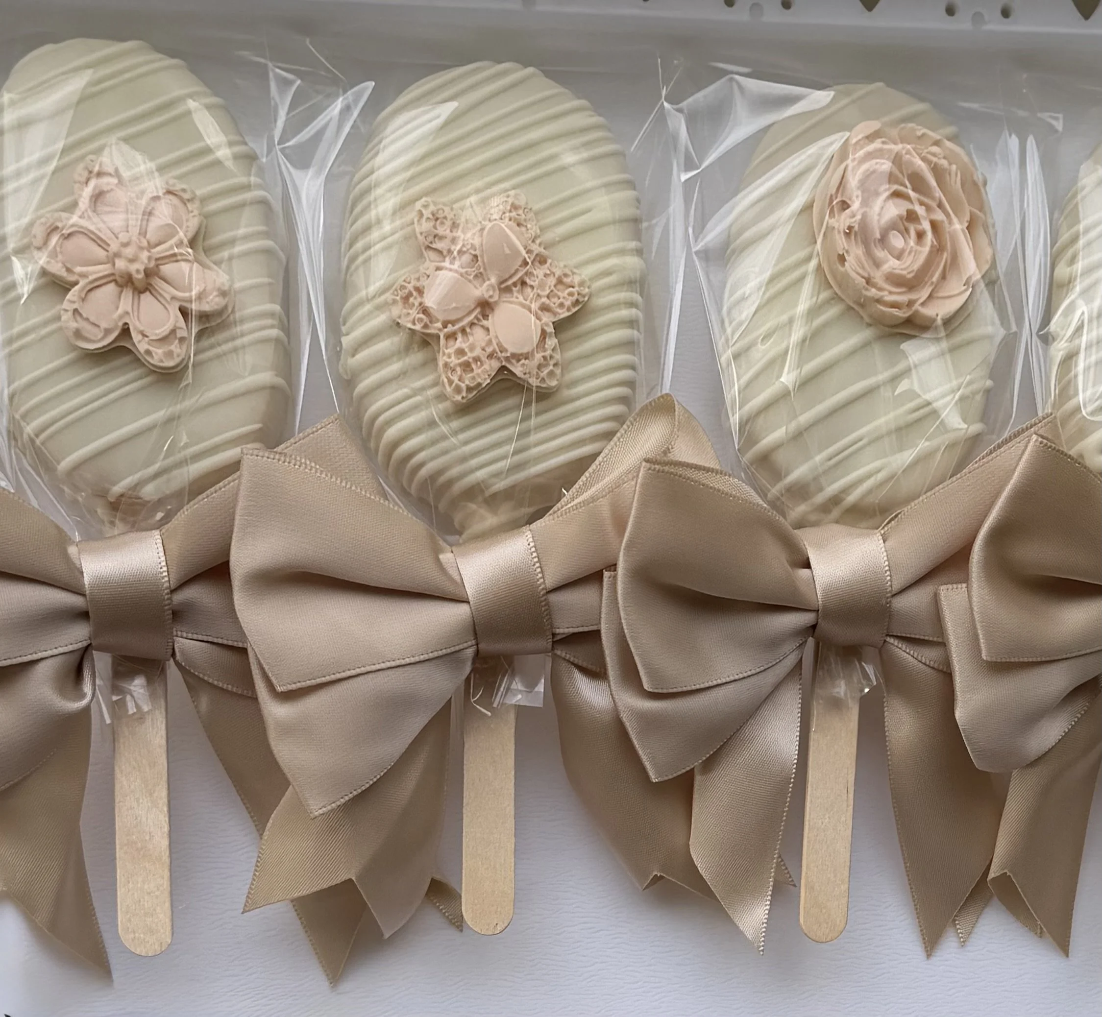 A row of packaged white chocolates with decorative flower and insect designs on top, wrapped in transparent plastic with beige ribbons.