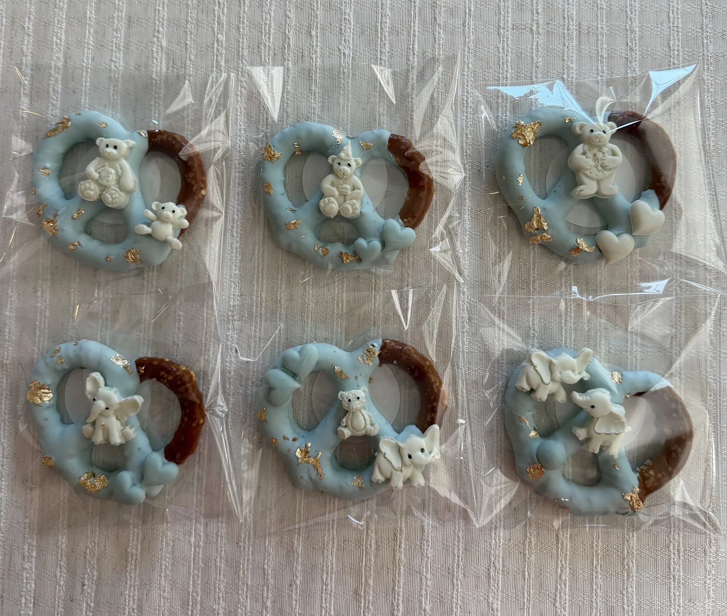 Decorated cookies with white bear and teddy bear shapes, blue icing, gold accents, and clear plastic wrapping on a textured white surface.