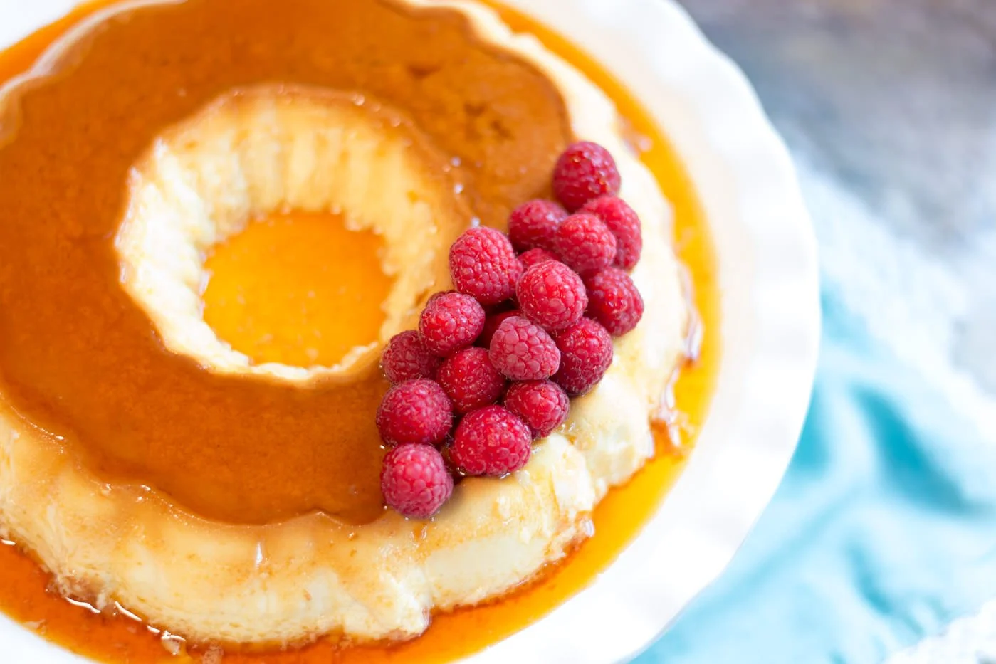 A close-up of a dessert with a caramel flan topped with raspberries and caramel sauce.