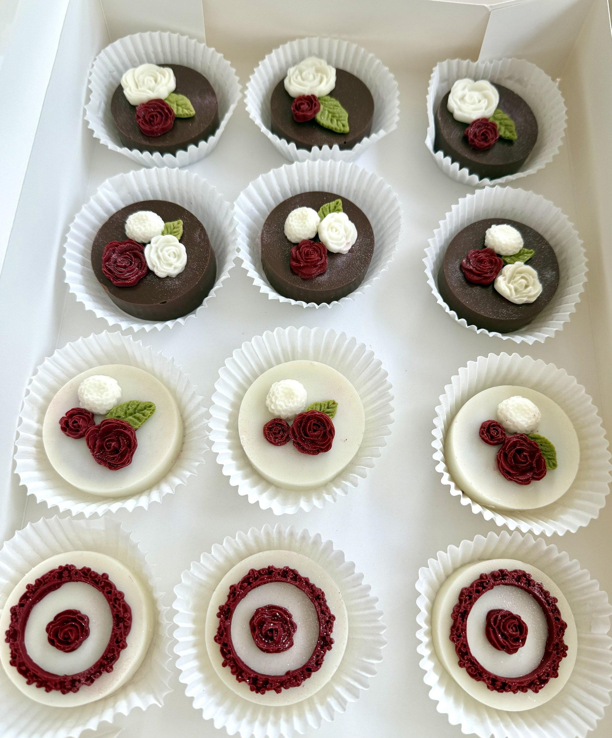 A dozen of chocolate dipped Oreo's decorated with red and white rose and leaf designs and white frames.