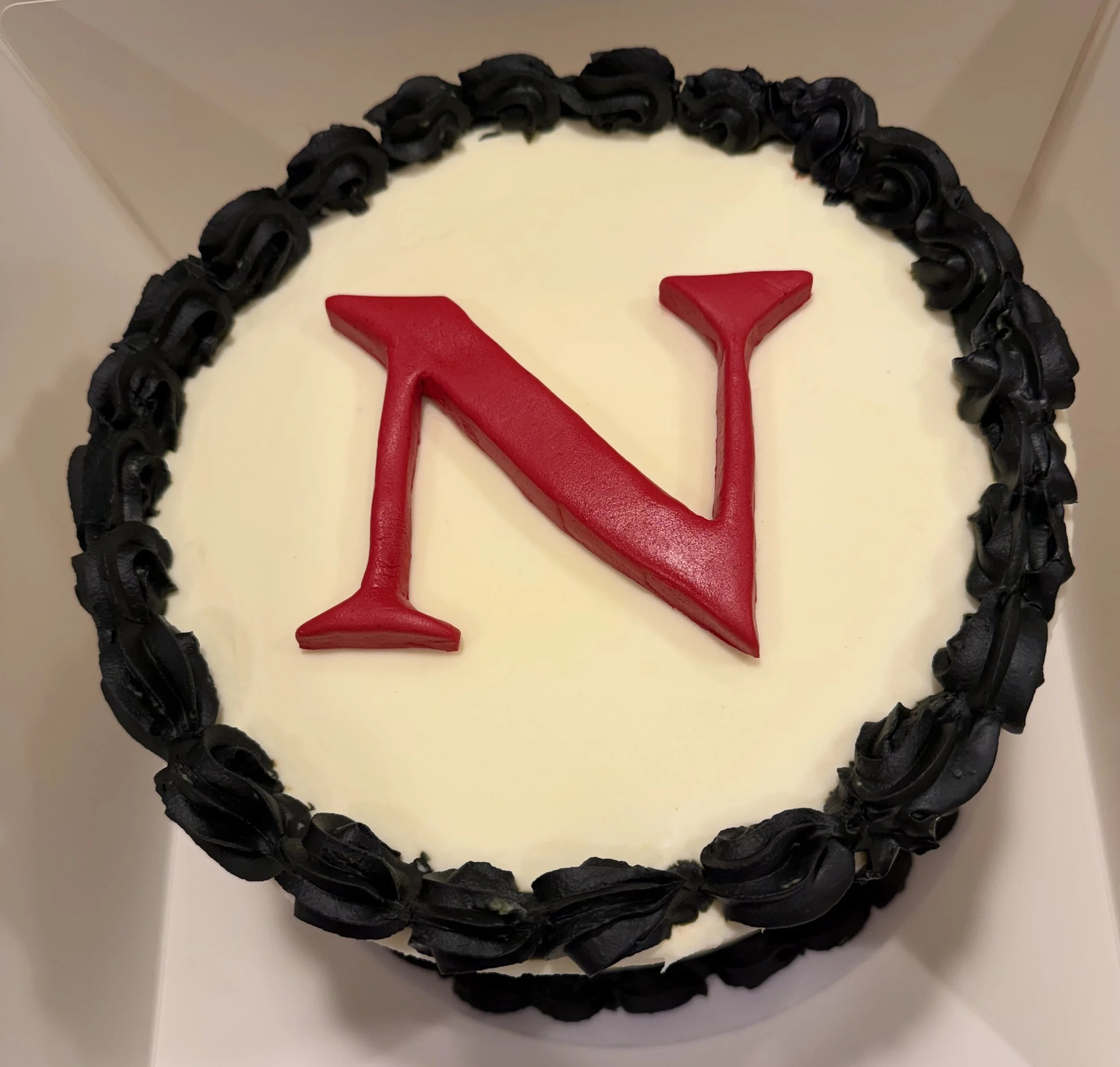 Graduation Northeastern N cake decorated with black piping frosting around the edges and red fondant letter N in the center. Strawberry filling 8" cake.