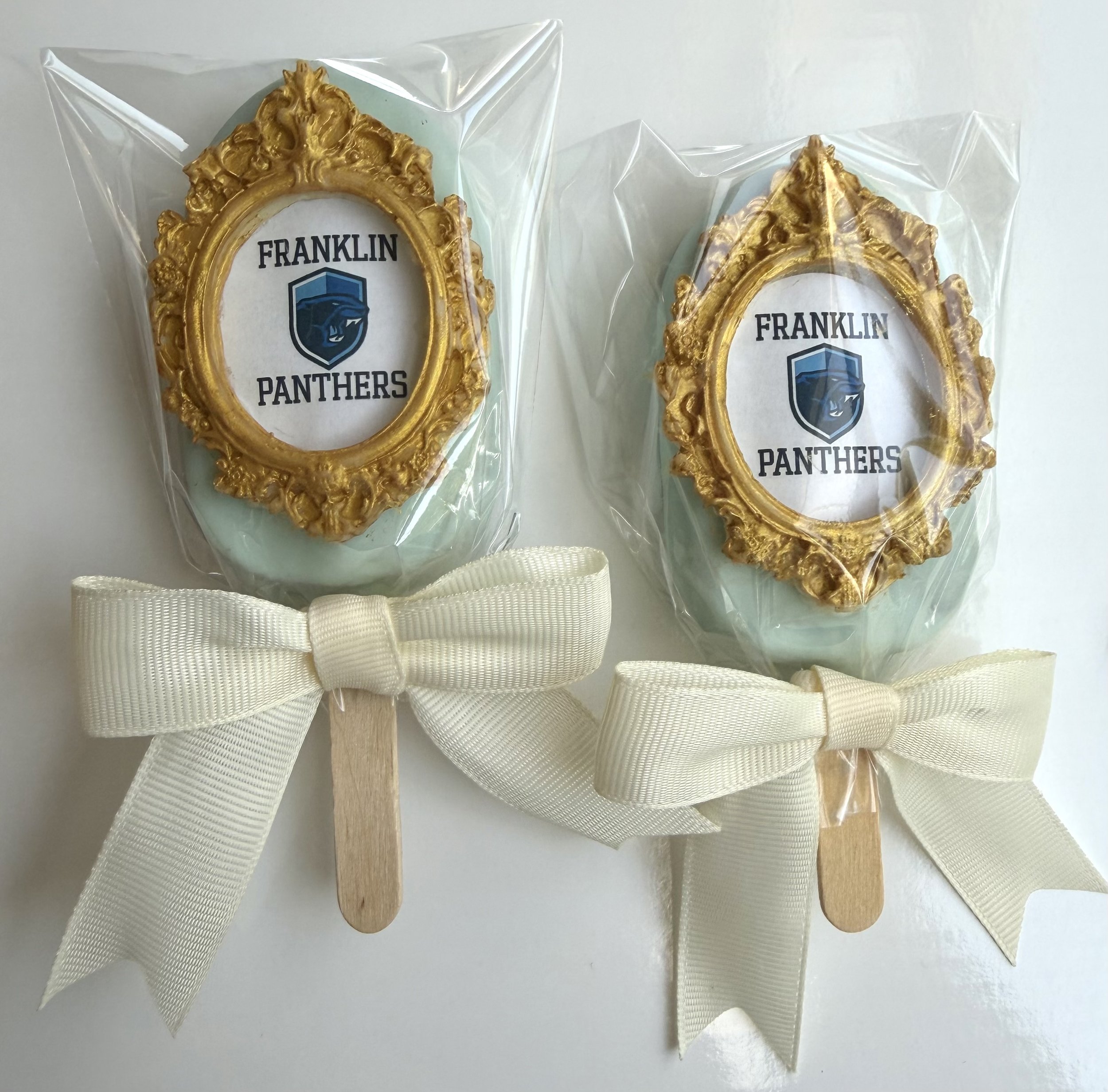 Decorative photo frame with the words Franklin Panthers and a panther logo, surrounded by gold ornate detailing, attached to a white ribbon and wooden sticks, all wrapped in clear plastic.