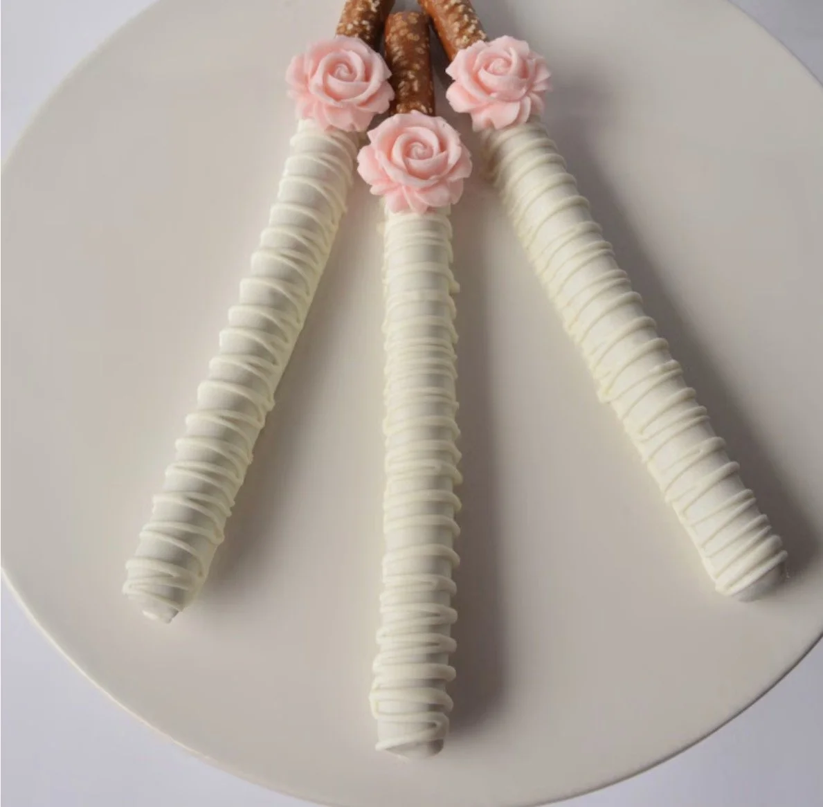 Decorative plate with three white chocolate-dipped pretzels, each topped with pink rose-shaped frosting.