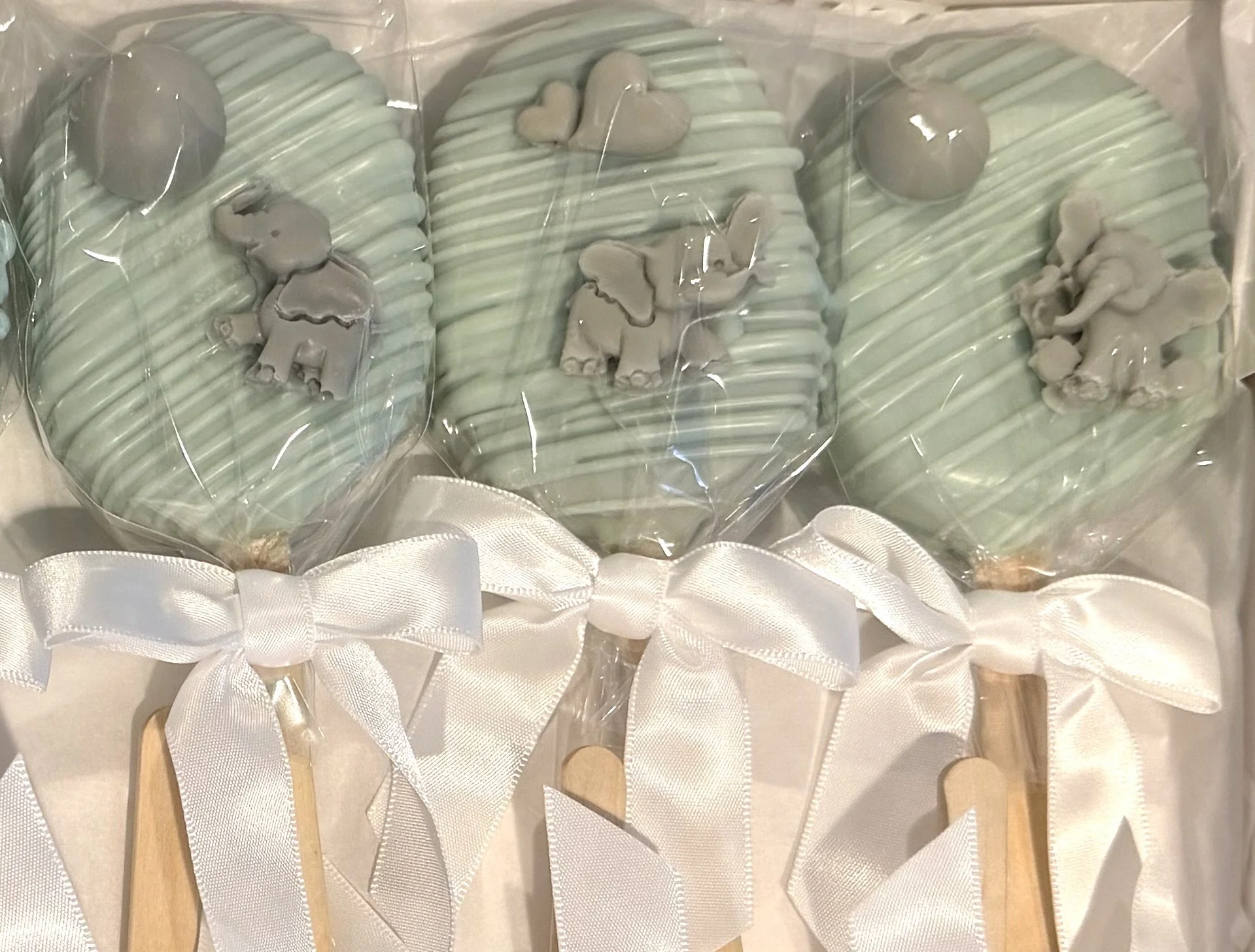 A set of mint green scented soap bars decorated with small dog and heart shaped soap embellishments, tied with white satin ribbons and attached to wooden sticks, arranged in a row for display or gift.