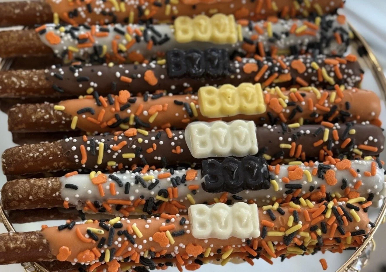 Colorful pretzel sticks dipped in chocolate, topped with sprinkles. It is a Halloween-themed candies for a Halloween celebration.