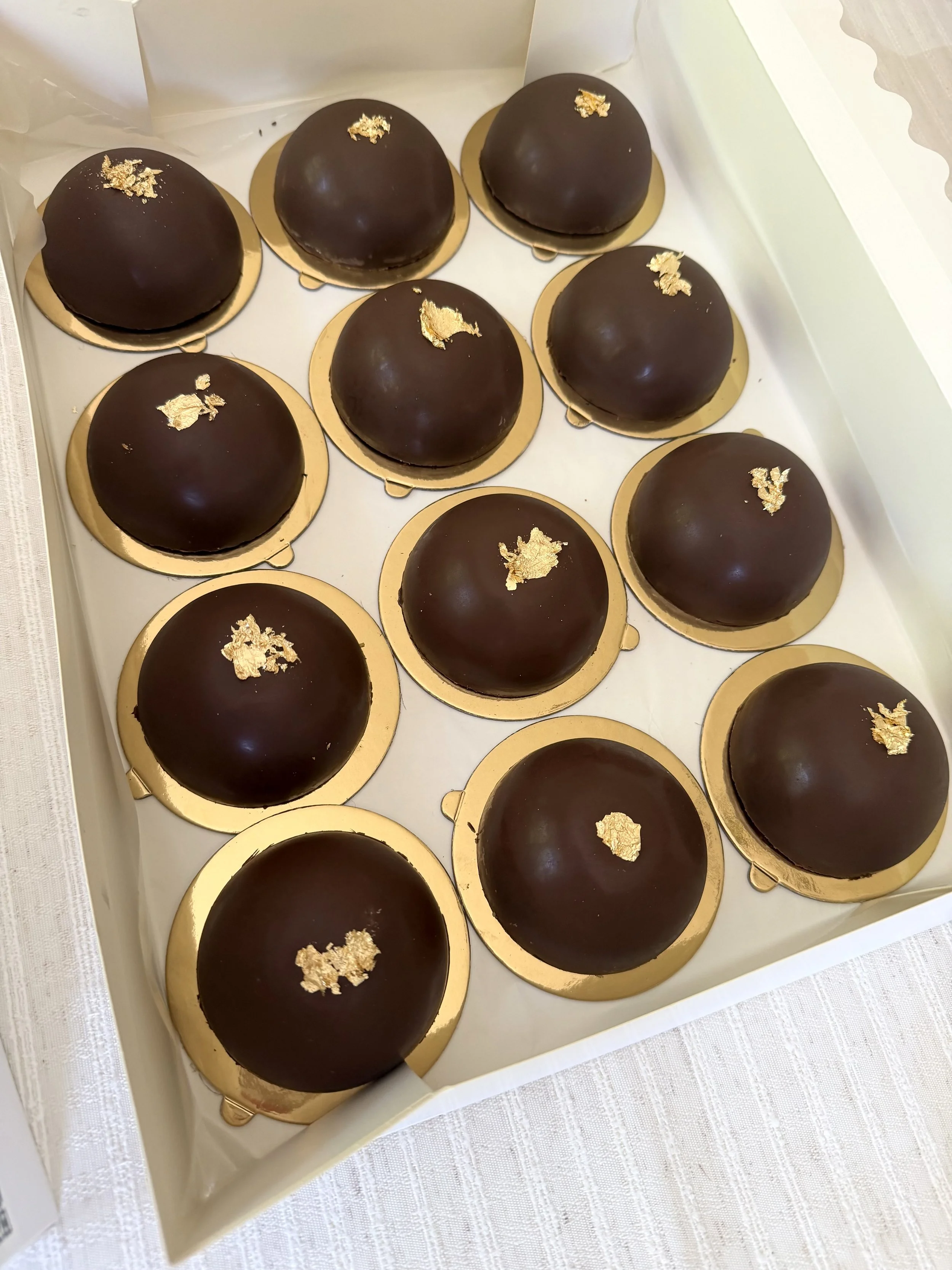 Box of dozen Dubai style pistachio dome, covered with chocolate and topped with small pieces of gold leaf.