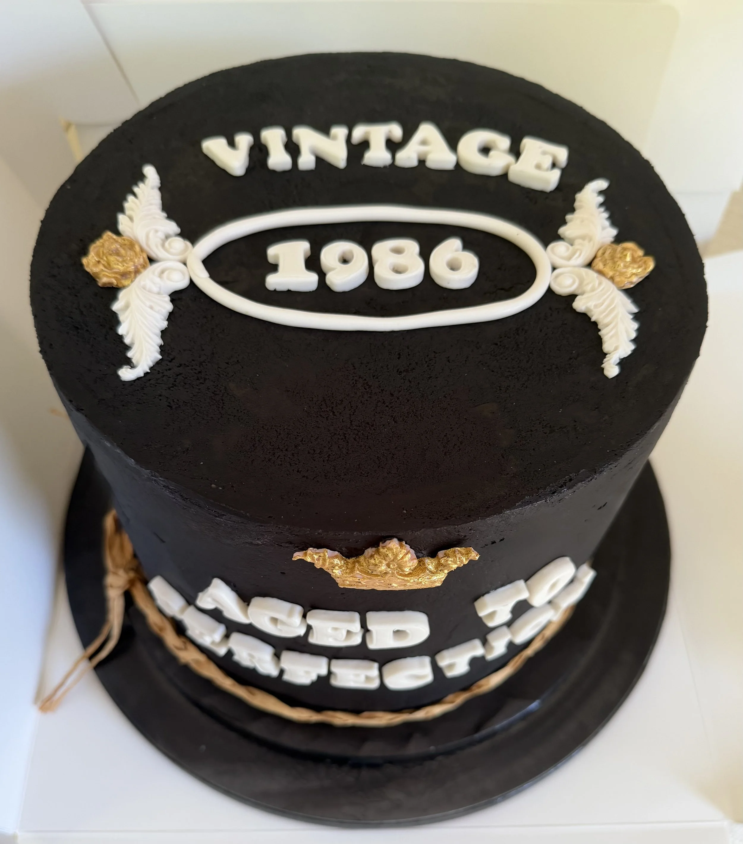 Round black birthday cake with white and gold decorations, featuring the words 'VINTAGE 1986' on top.