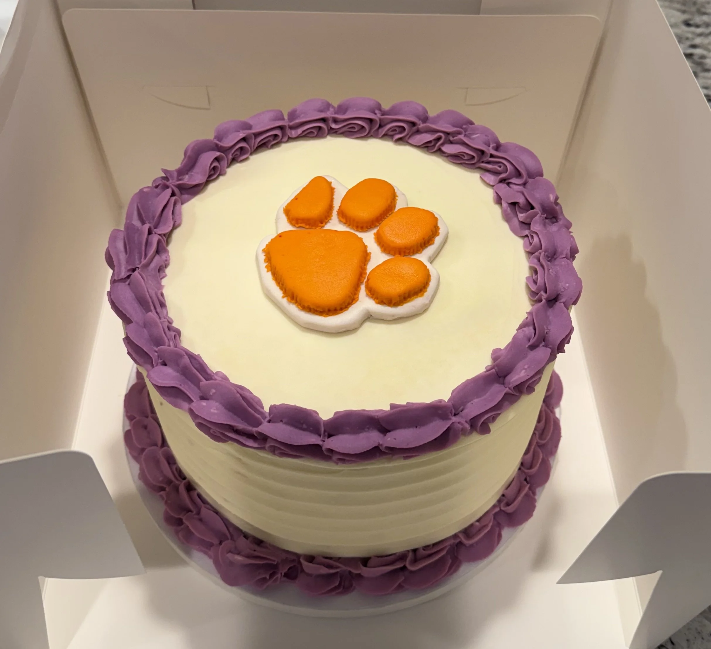 An 8" cake with Clemson orange paws decorated with purple piping along the top and bottom.