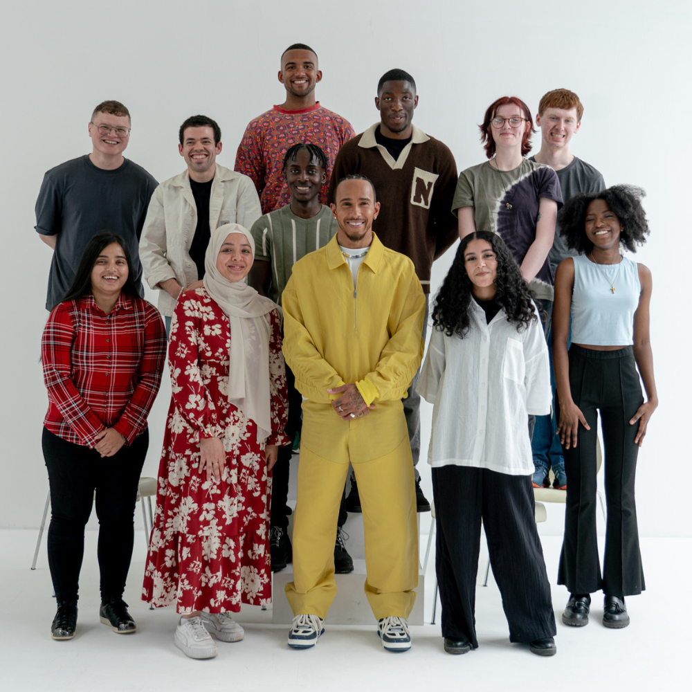 A diverse group of 13 young adults posing together against a plain white background.