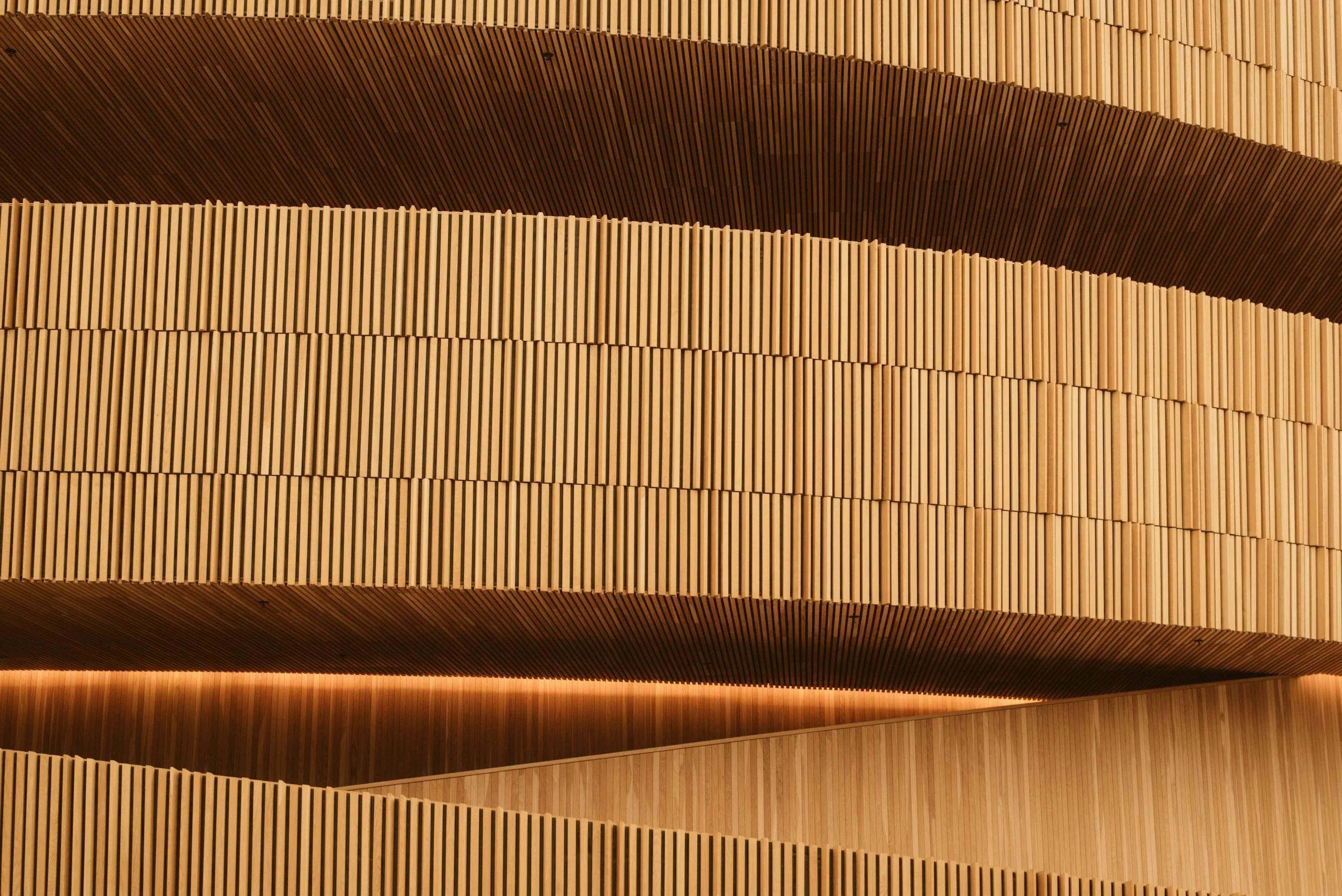 Nahaufnahme einer strukturieren Holzdecke mit schmalen senkrechten Lamellen in unterschiedlichen Höhen, beleuchtet von unten