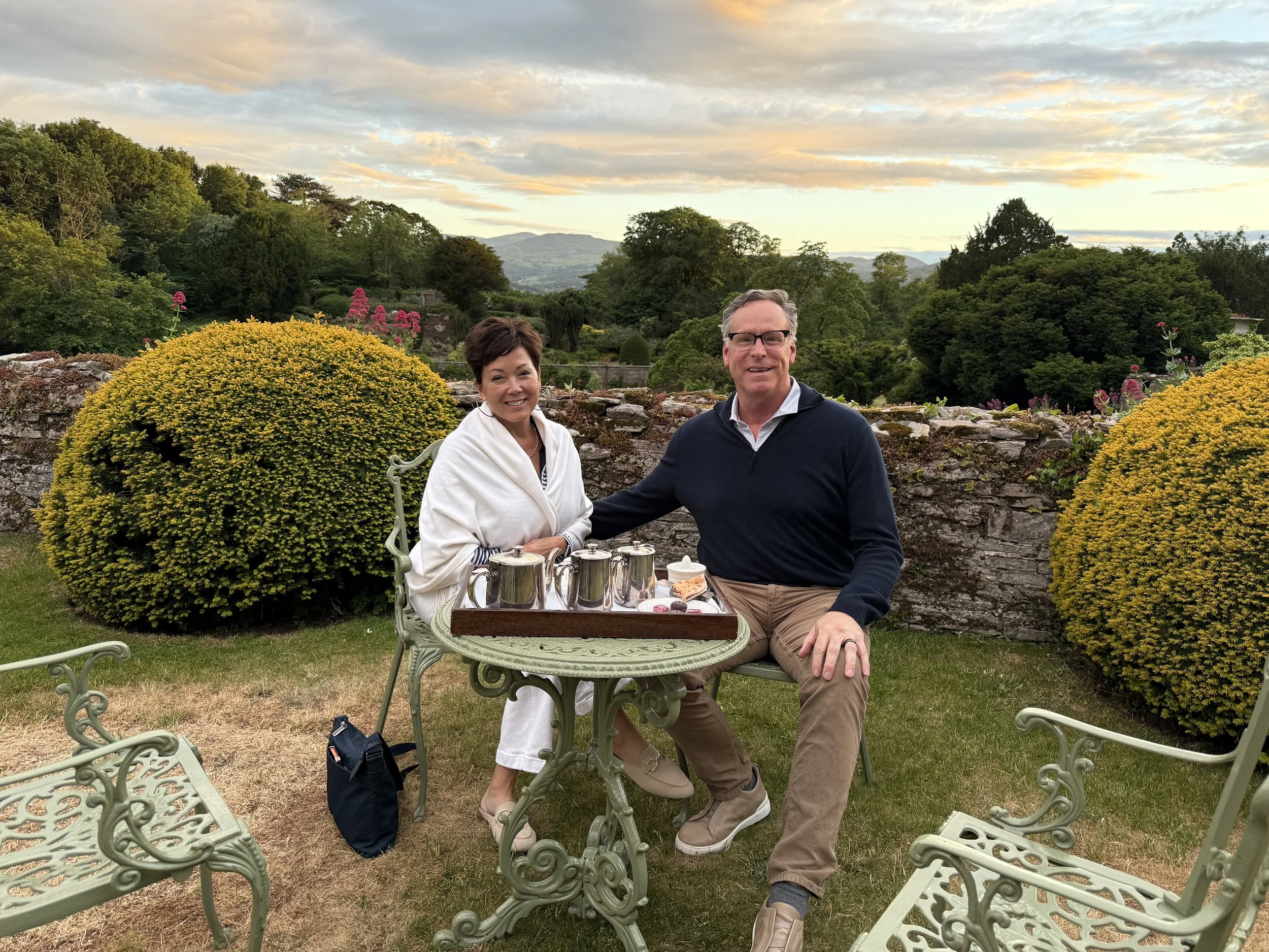 Susan and Scott smiling in golden-hour light with Bodysgallen Hall behind them