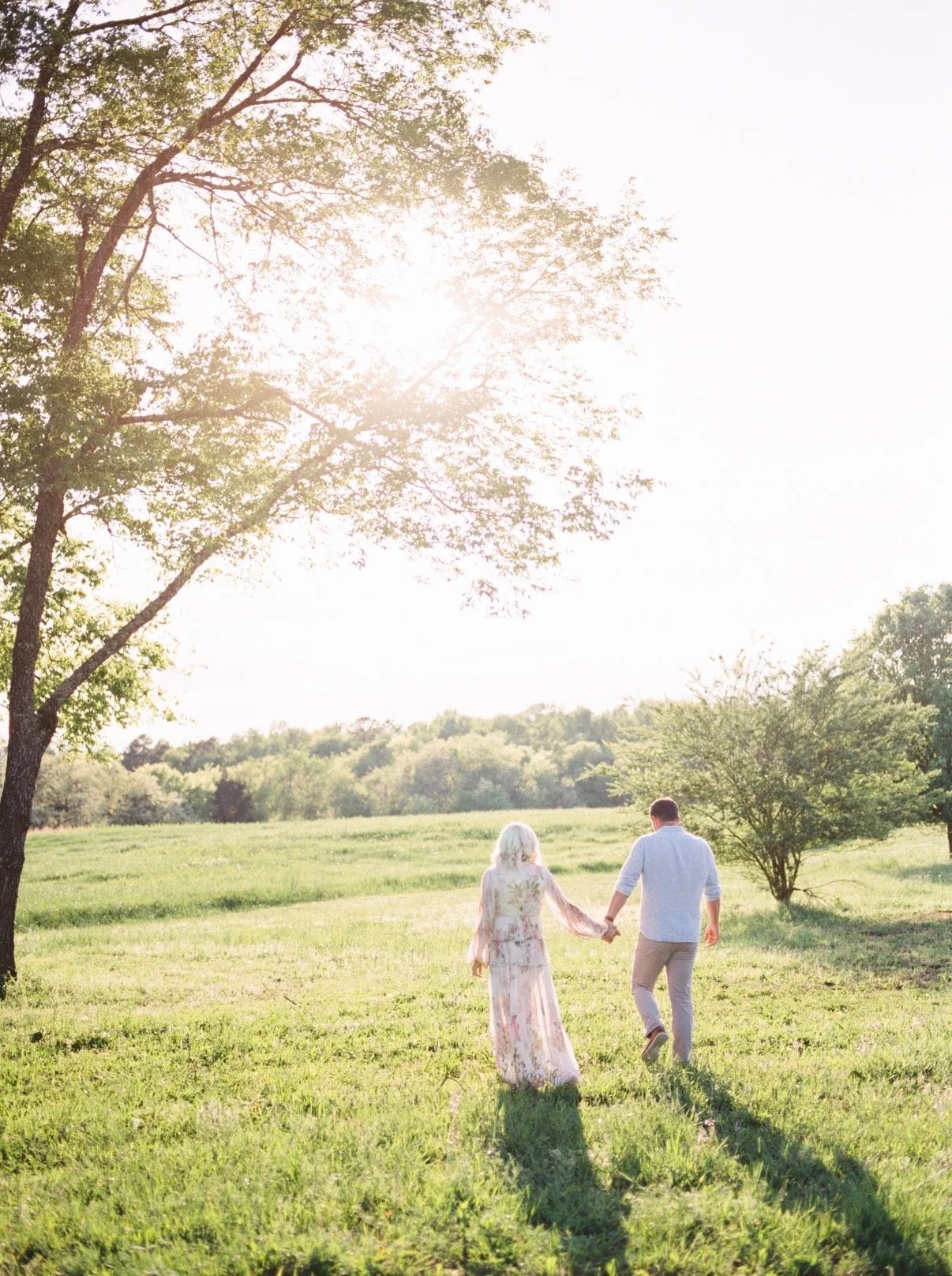 Couple holding hands while walking through field.