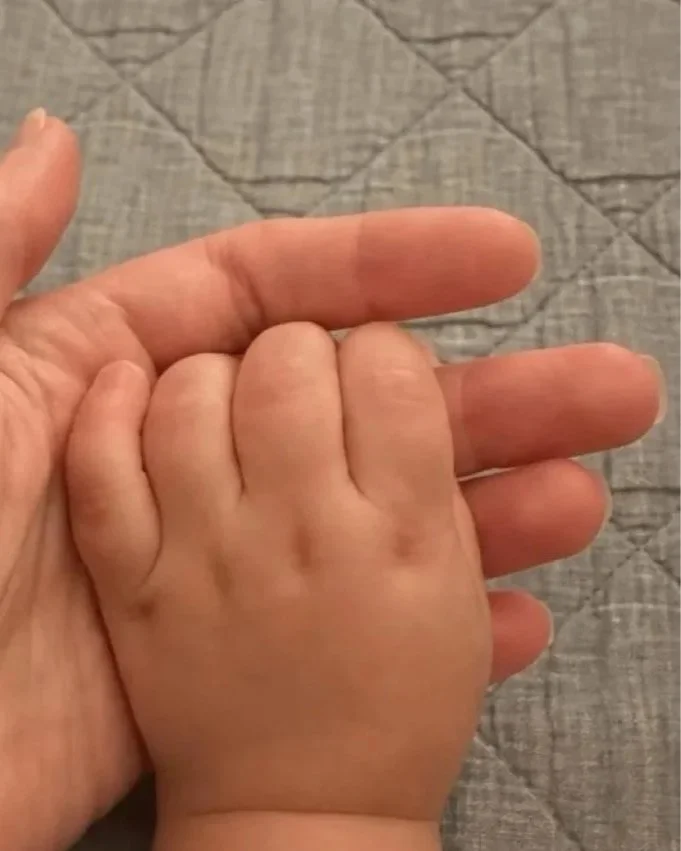 Adult hand gently holding a baby's hand.