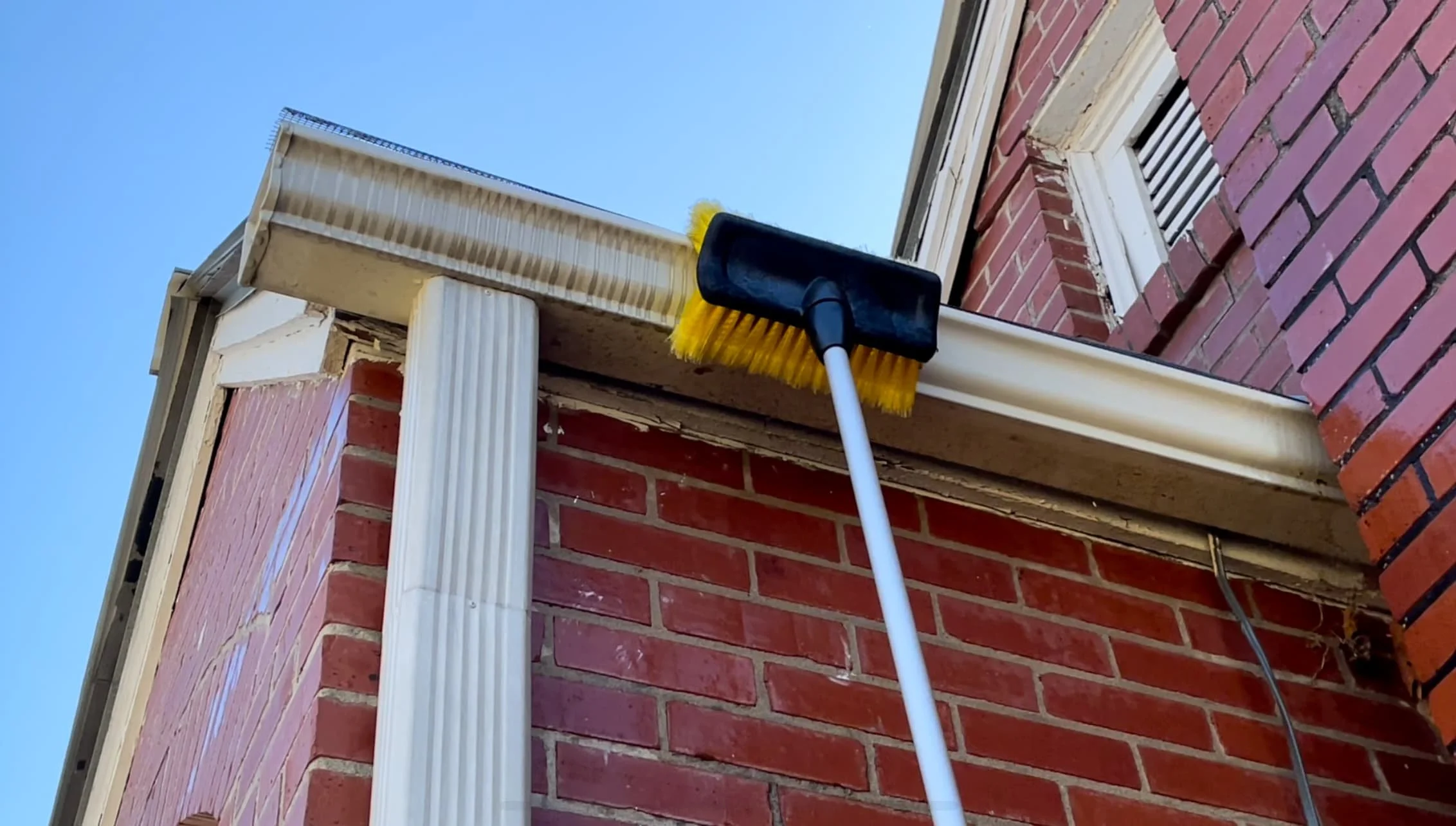 Gutter cleaning removing oxidation from aluminum gutters. The image shows a gentle brushing after applying a cleaning solution to remove stubborn buildup.