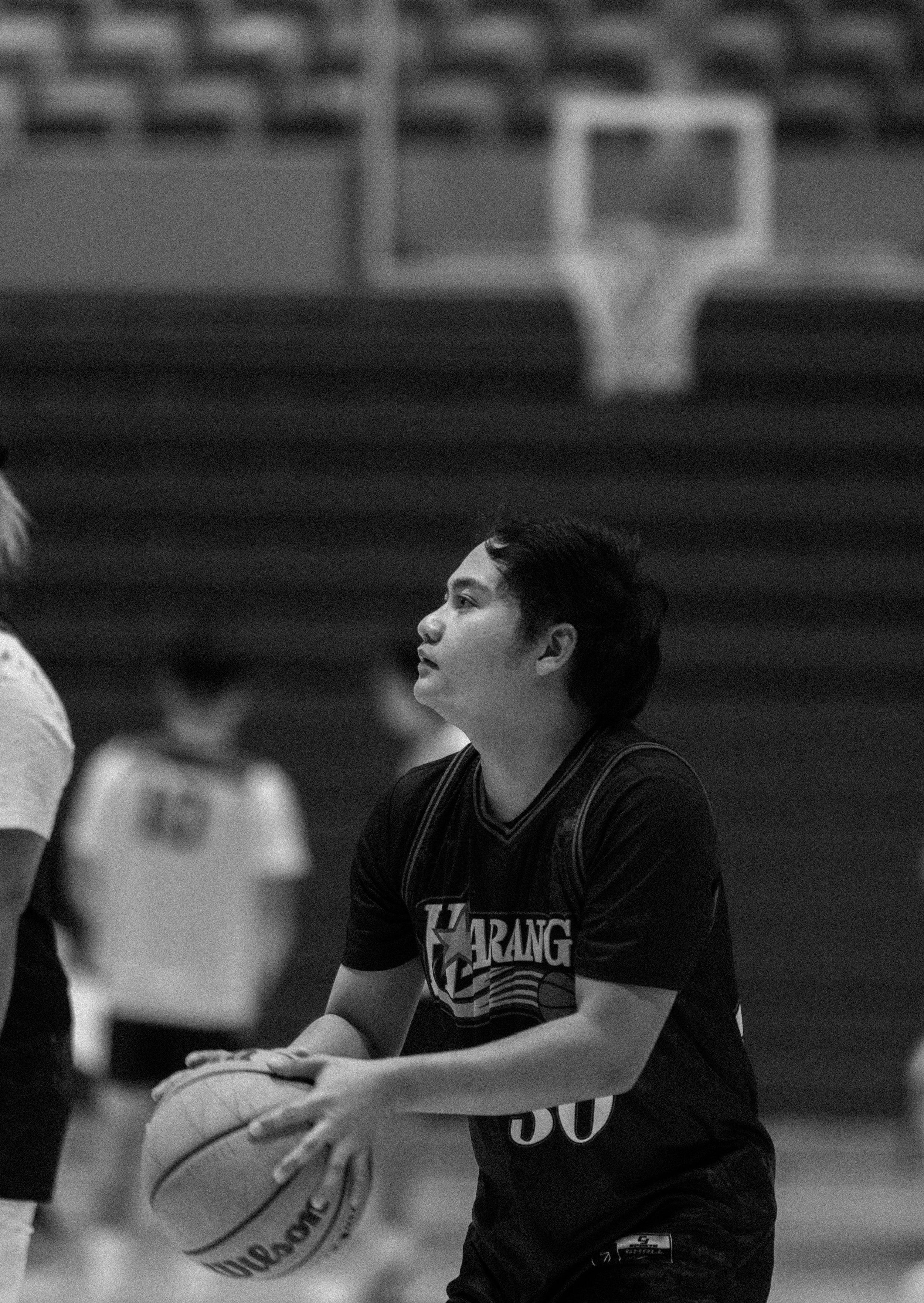A young man preparing to shoot a basketball on an indoor court. He is wearing a black sports jersey with the number 30.