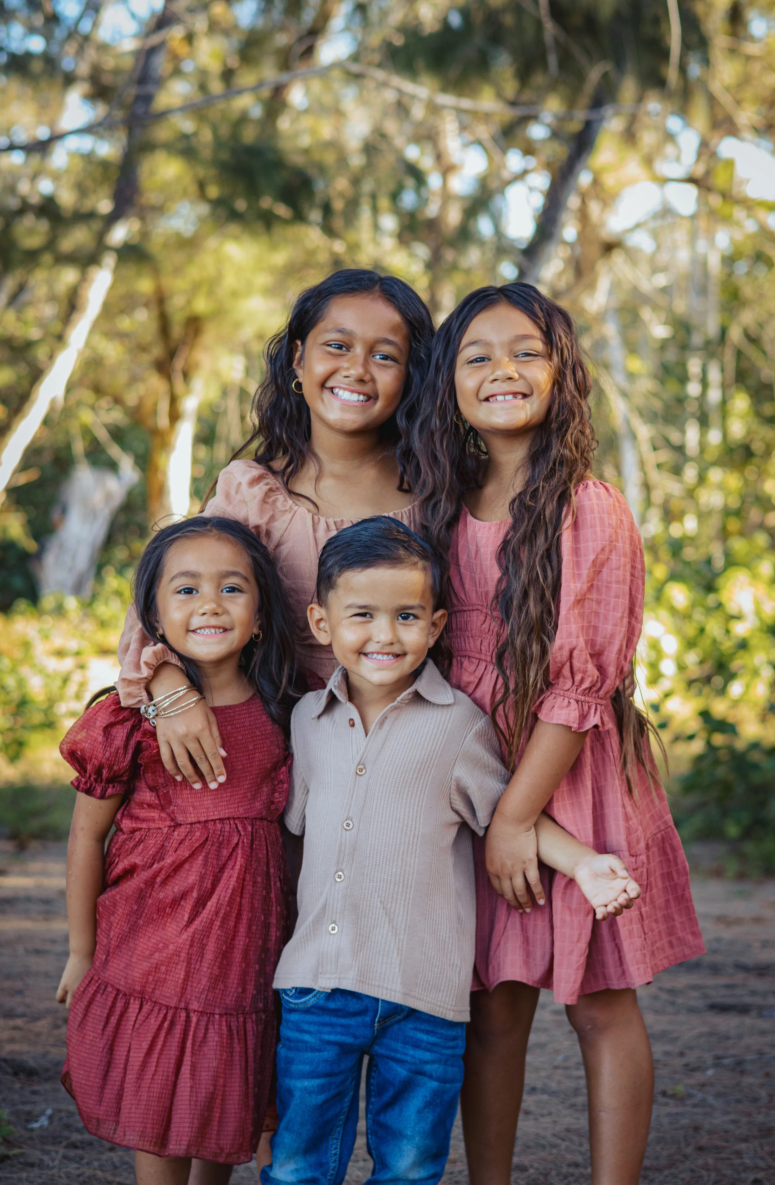 Five children smiling outdoors in a wooded area, standing close together.