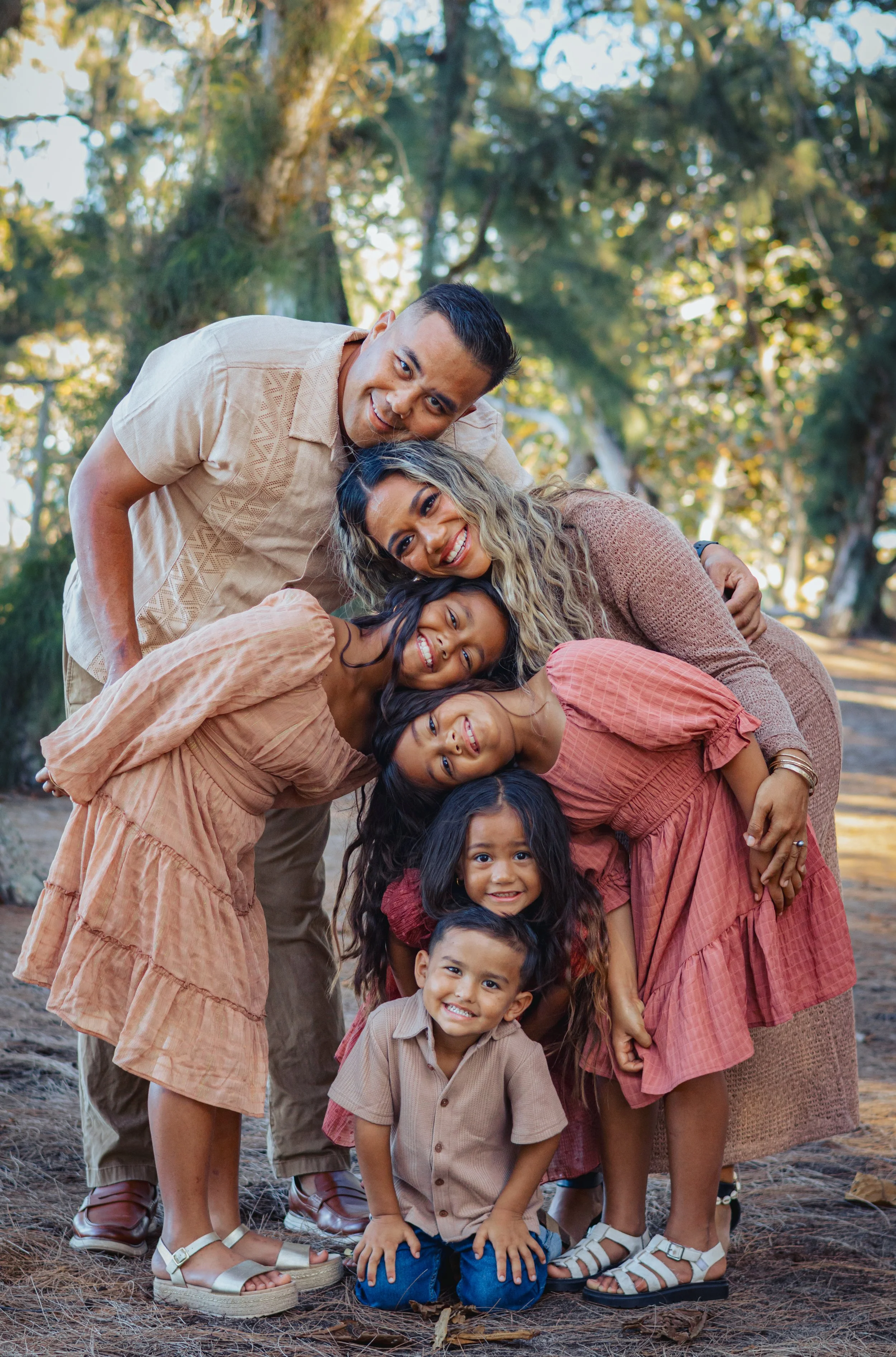 Family of seven in a forest during daytime, smiling and leaning together.