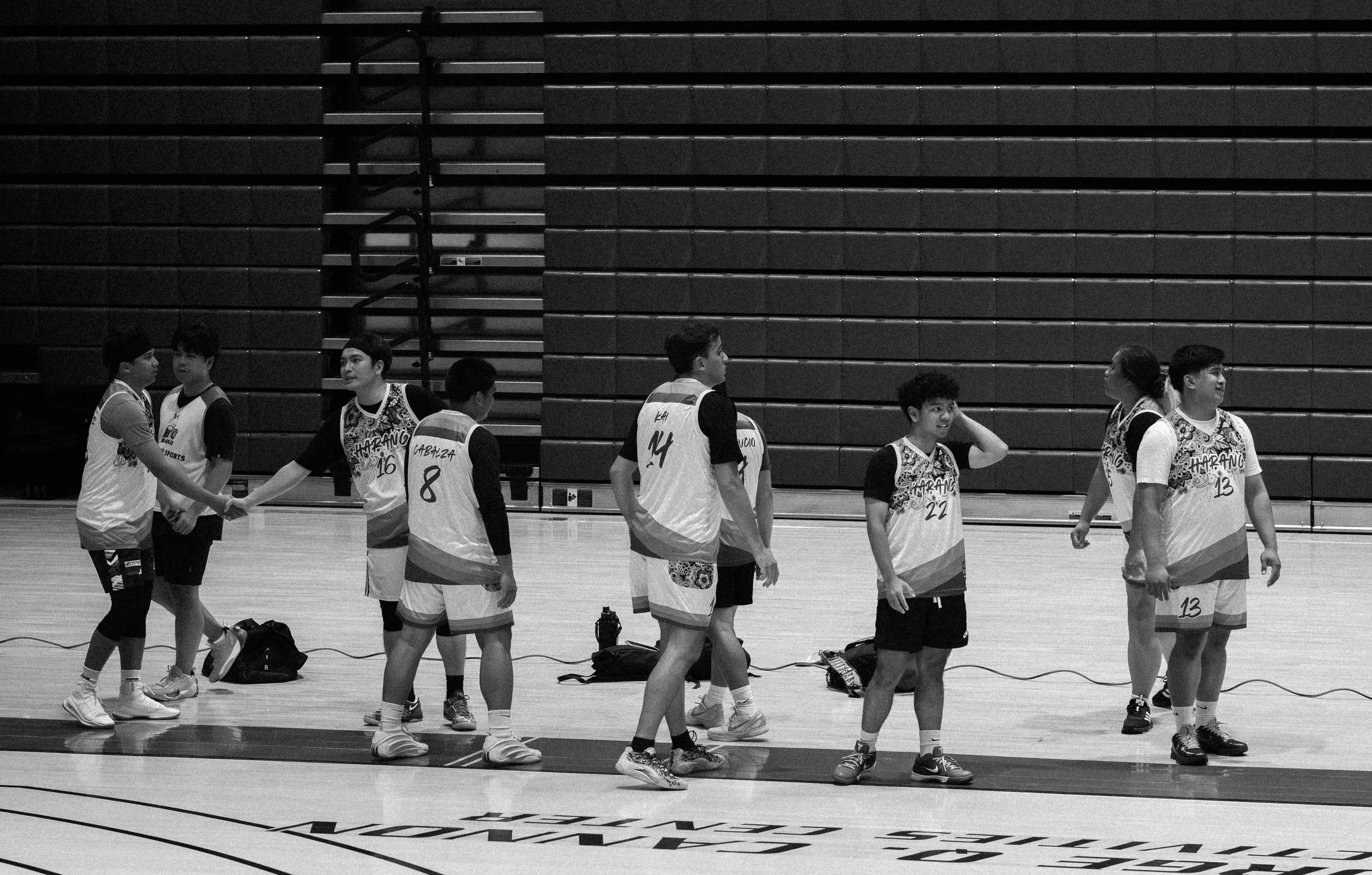 A group of young basketball players standing on a basketball court during a game or practice, shaking hands and interacting, with equipment bags on the floor.