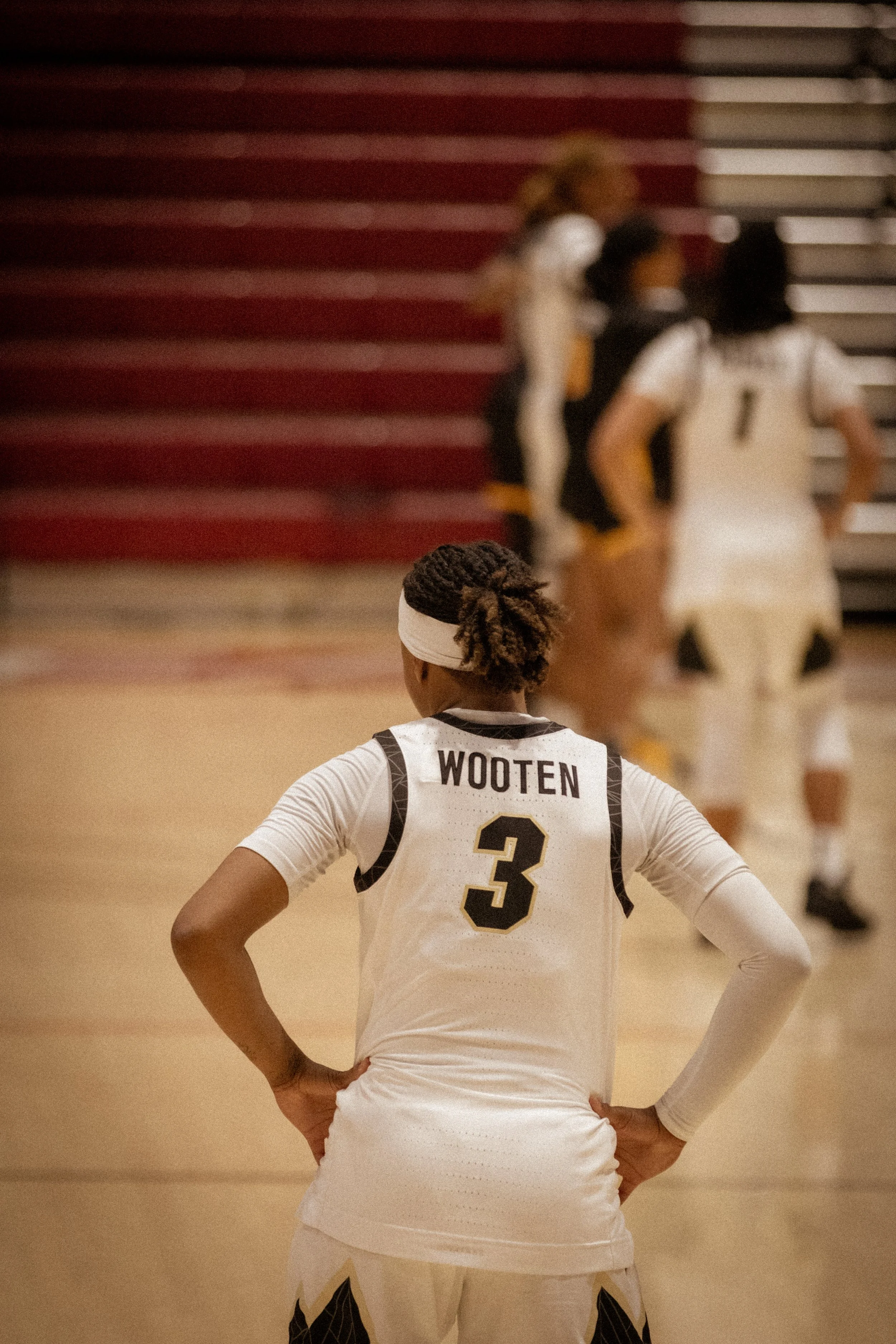 A female basketball player with jersey number 3 named Wooten standing on the court with her hands on her hips, facing away from the camera, during a game.
