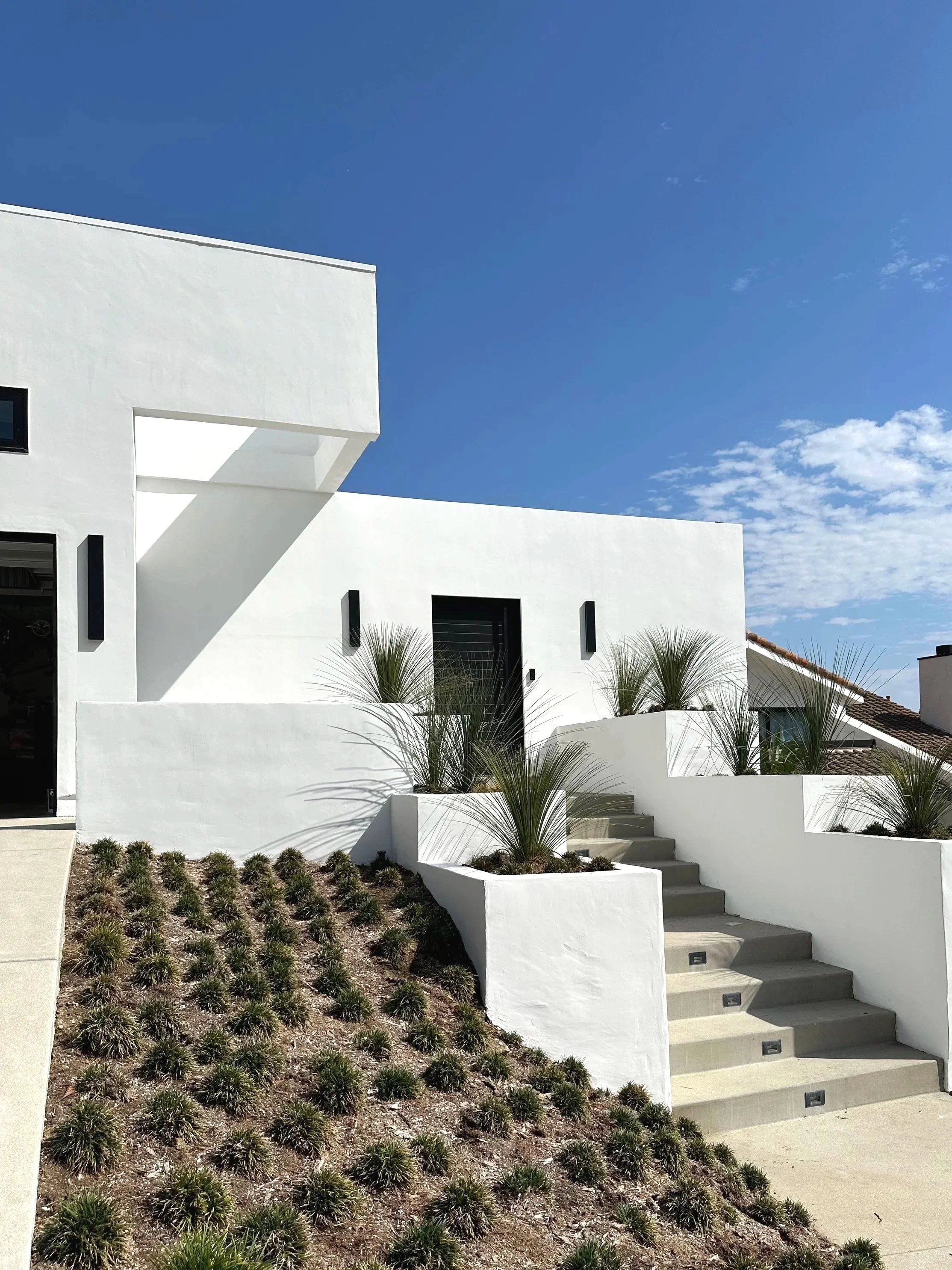 Modern white house with stairs leading up to the entrance, desert plants and clear blue sky.