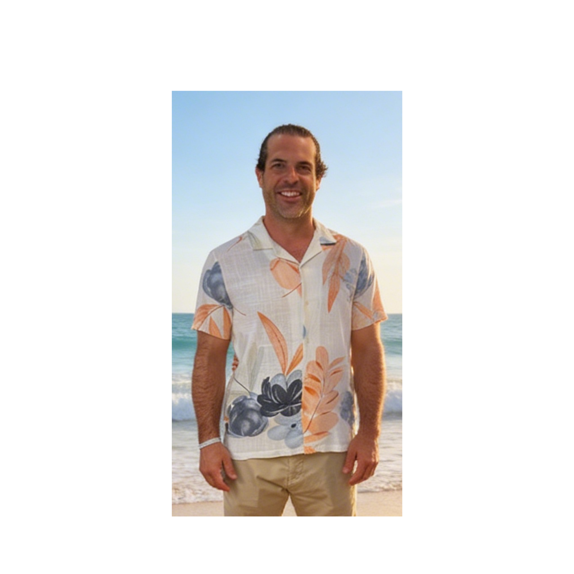 A man standing on a beach, smiling, with the ocean and sky in the background. He is wearing a Hawaiian shirt with floral patterns and khaki shorts.
