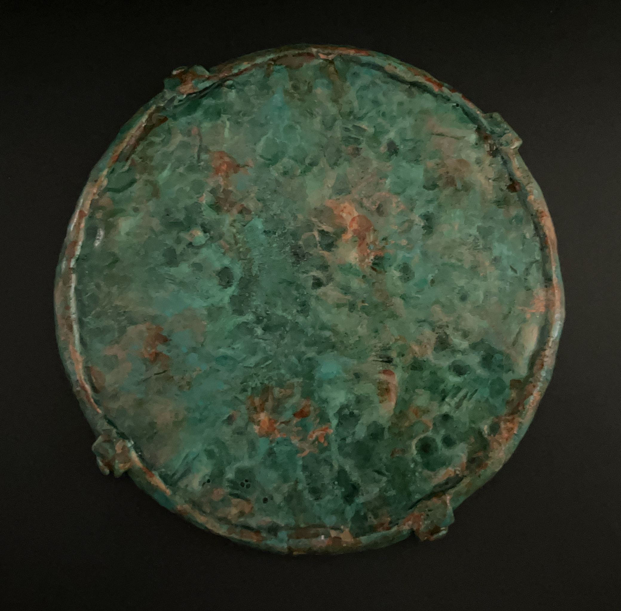 Close-up of a greenish, textured, and irregularly shaped metal object against a black background.