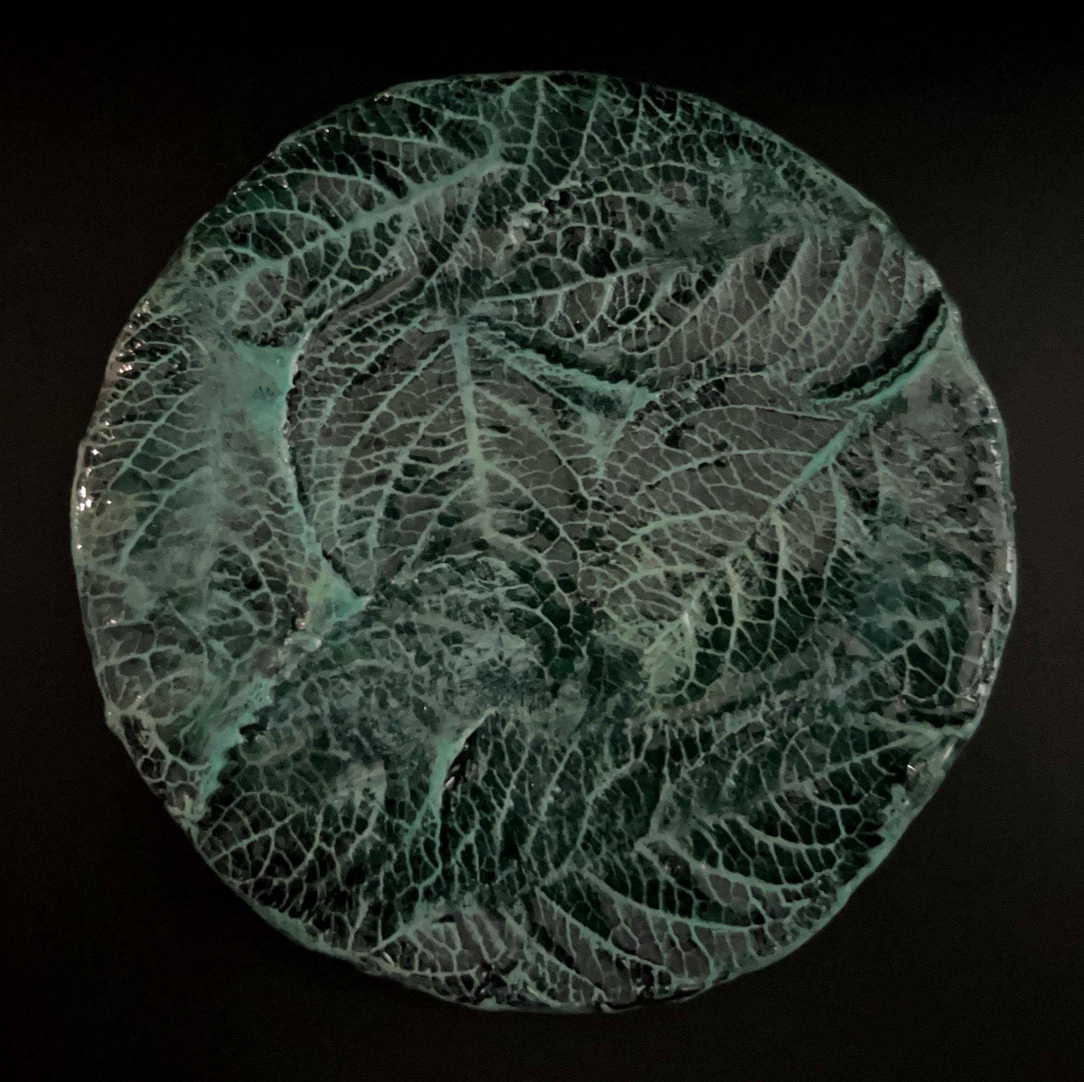 A glass sculpture of a leaf with intricate vein details, illuminated against a dark background.