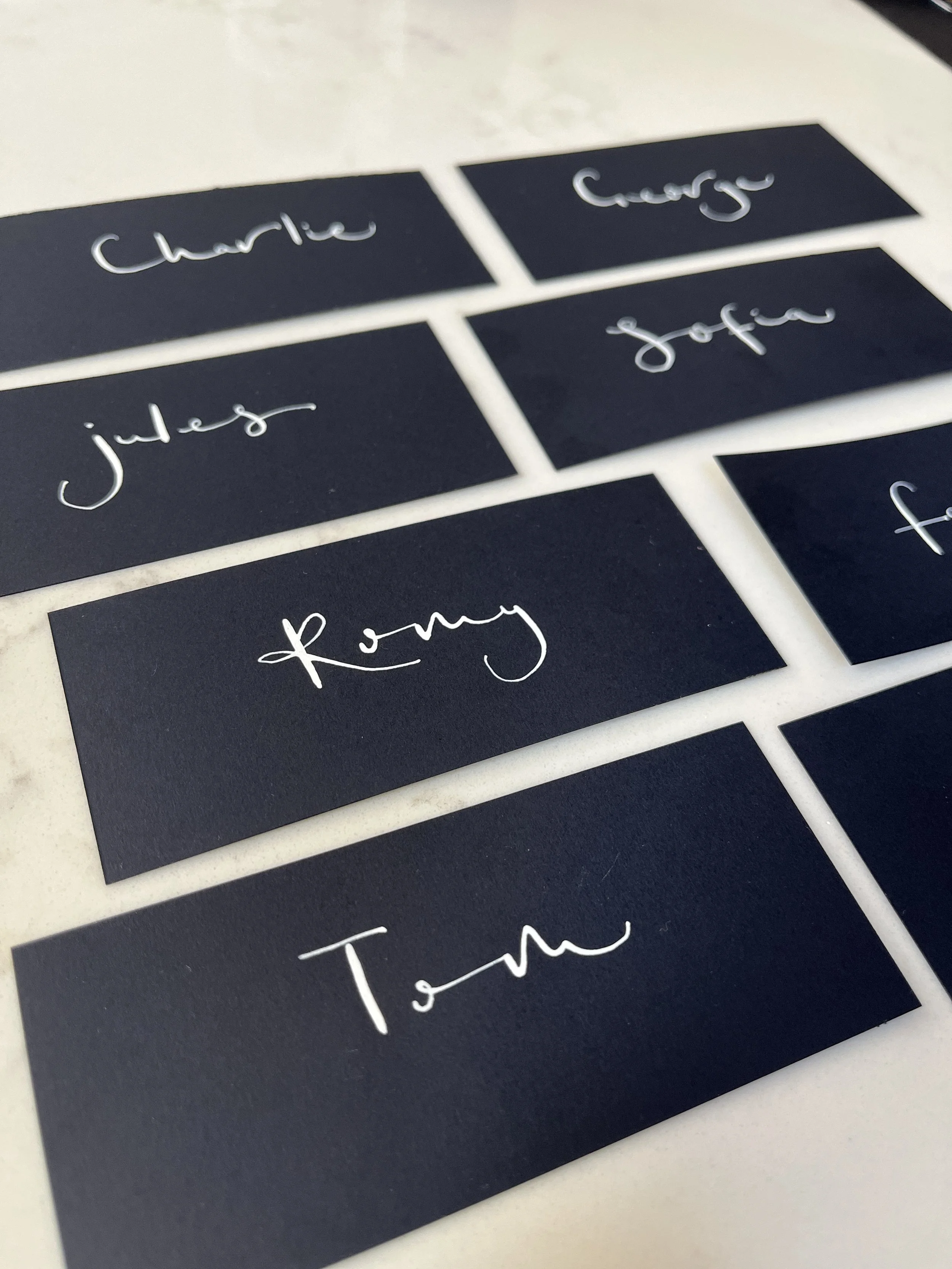 Dark blue place cards with white calligraphy writing for Charlie, George, Jules Sofia and Tom.
