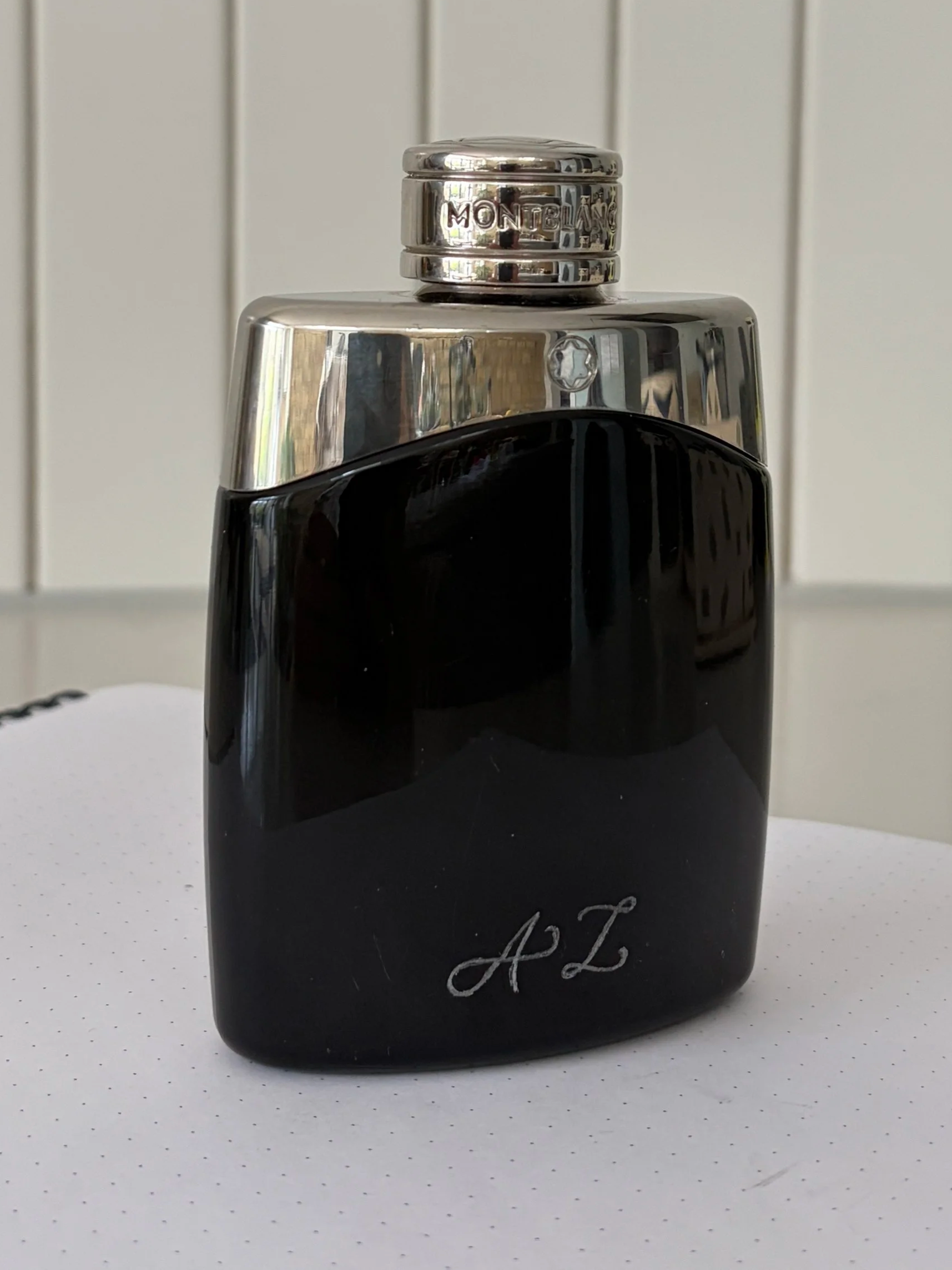 A black and silver aftershave bottle with initials 'A Z' engraved on it, placed in front of a tiled wall background