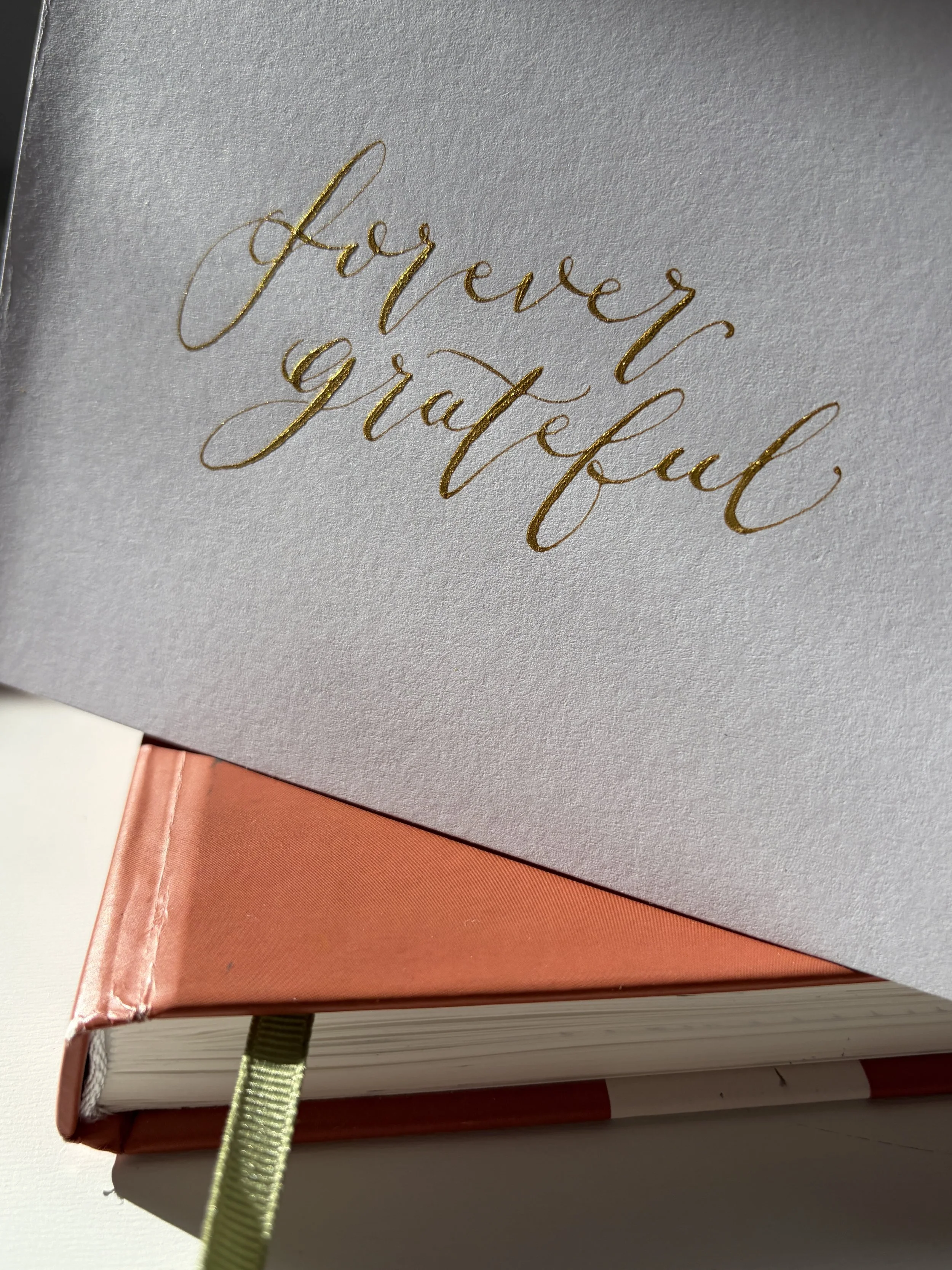 	
Close-up photo of a greetings card with gold calligraphy wording "forever grateful". The greetings card is sitting on a closed notebook.