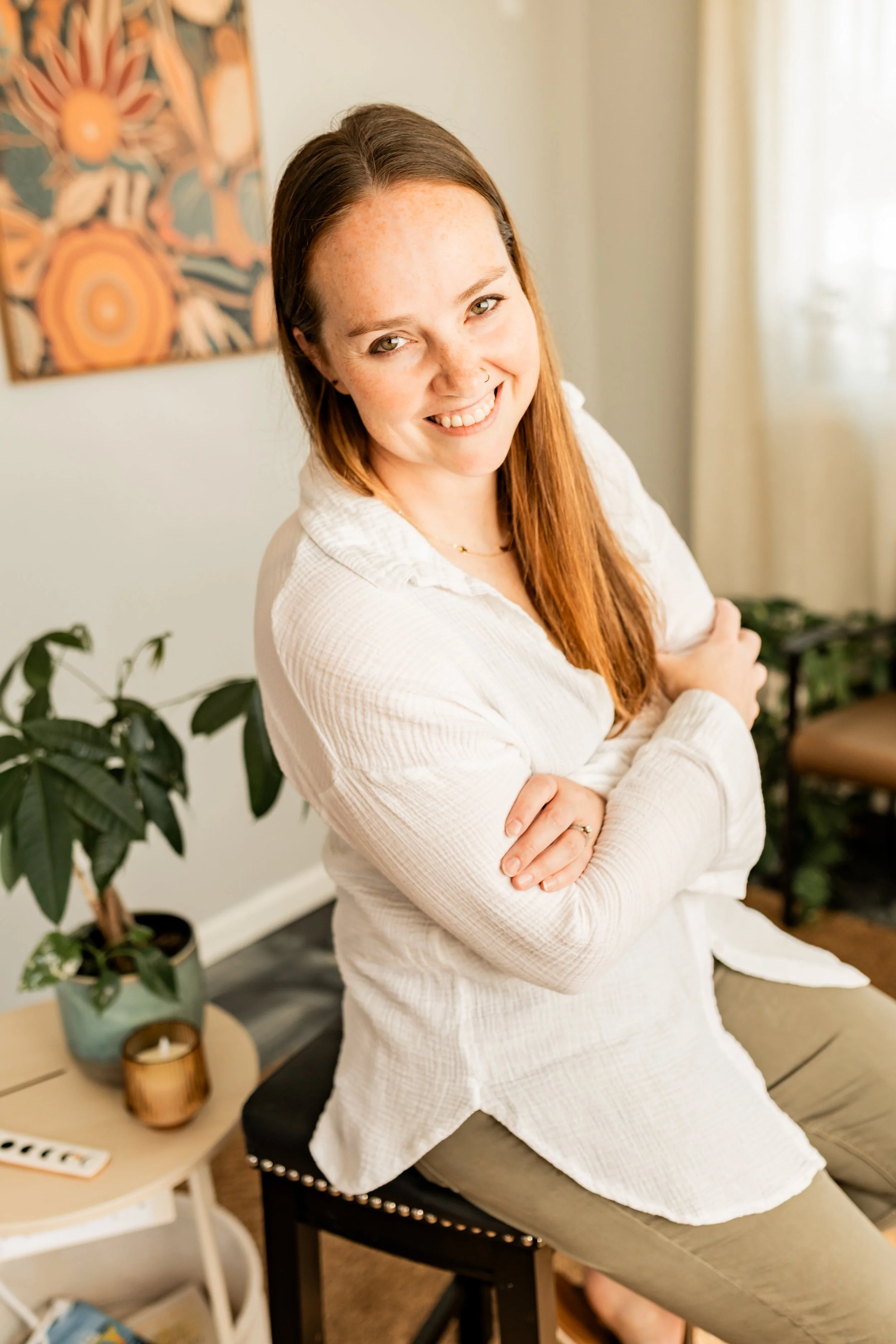 Katie Tyrrell smiling with her arms crossed, wearing a white top in a therapy office.