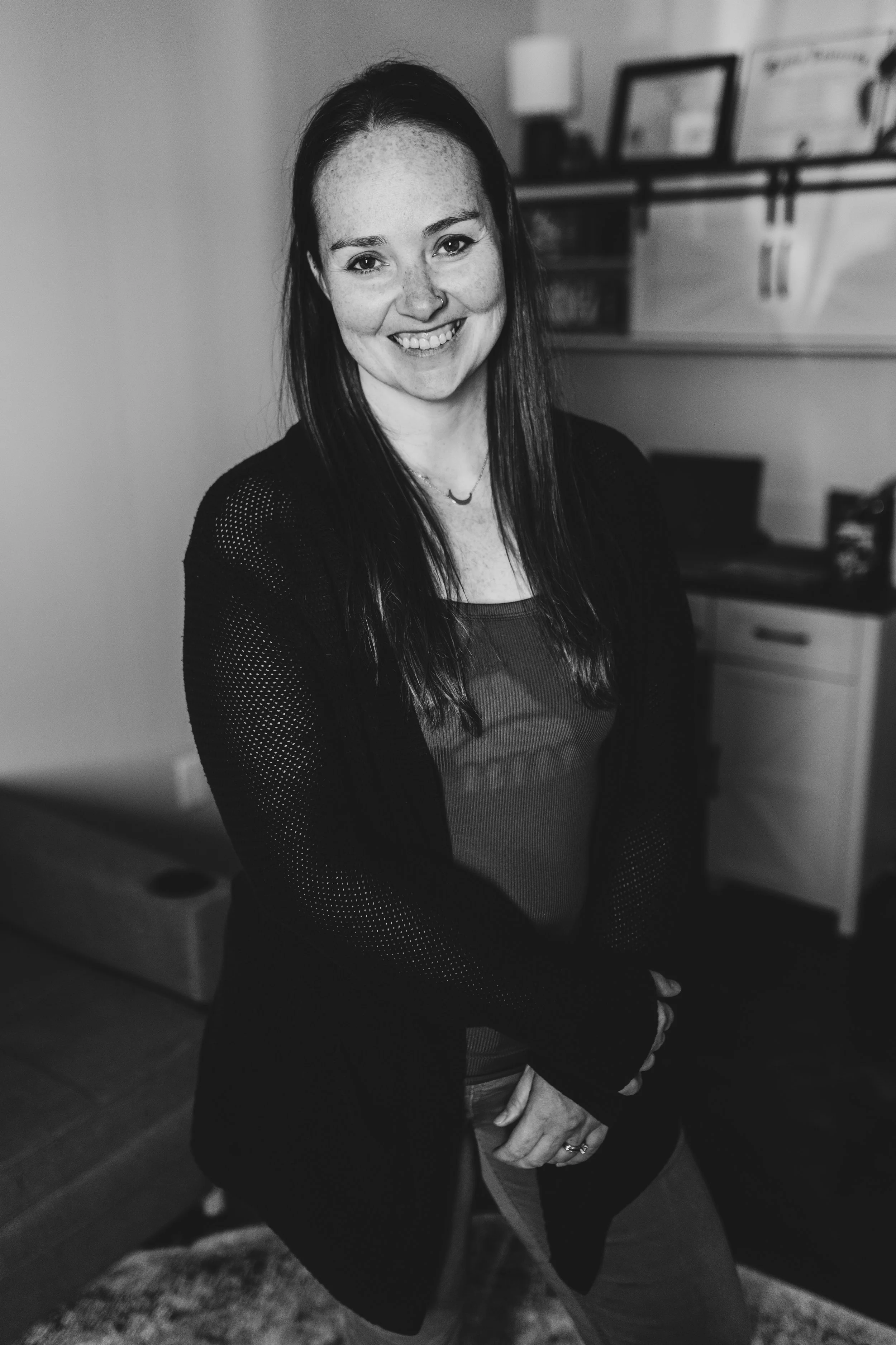 Katie Tyrrell smiling at the camera in her office, with a desk and framed artwork behind her.