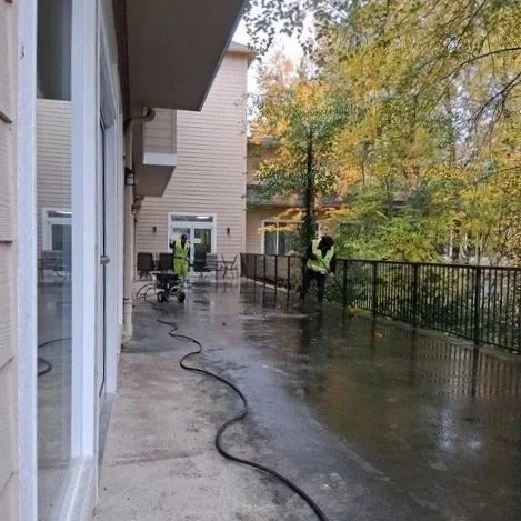 ESNTL Services team cleaning a wet walkway outside a building with trees and autumn foliage in the background.