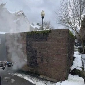 Steam or smoke rising from a damaged brick wall with snow on the ground and a streetlamp nearby.