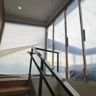 Interior view of a staircase with metal handrails next to large glass windows covered with plastic sheeting during construction or renovation.